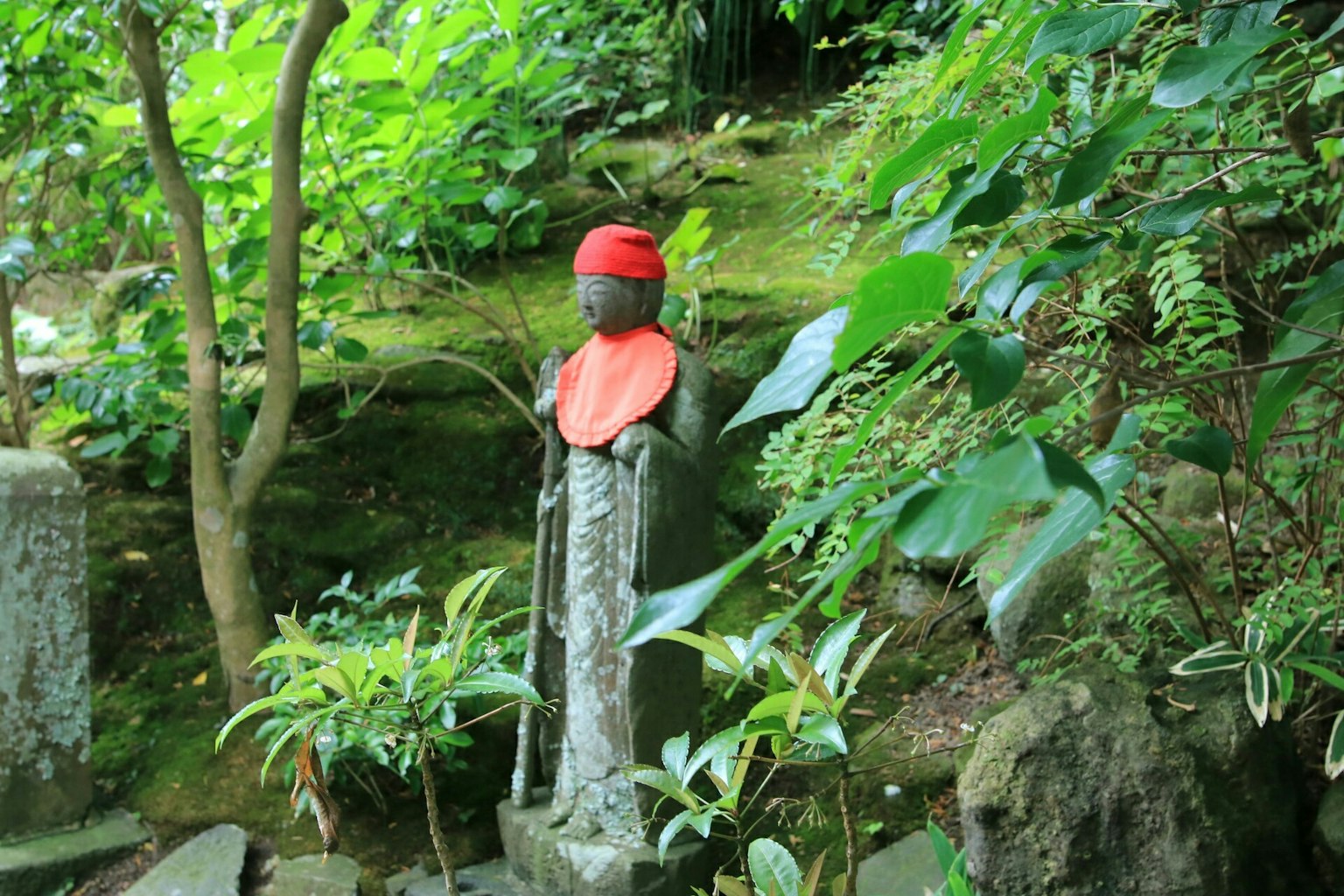 รูปปั้นหินที่ล้อมรอบด้วยพืชสีเขียวสวมหมวกแดงและเสื้อผ้าแดง