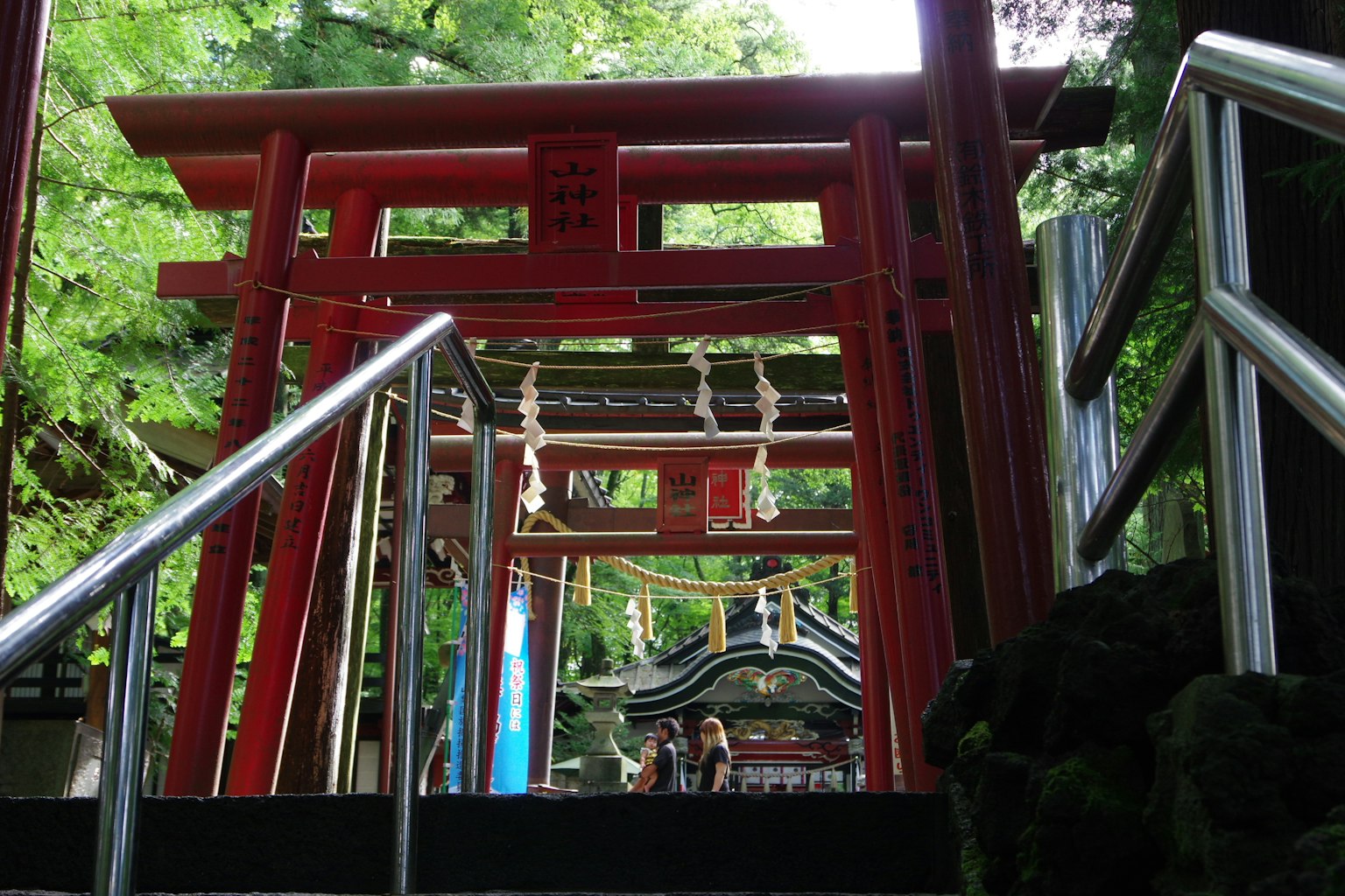 Cảnh cổng vào của một ngôi đền với cổng torii đỏ và cây xanh ở phía sau