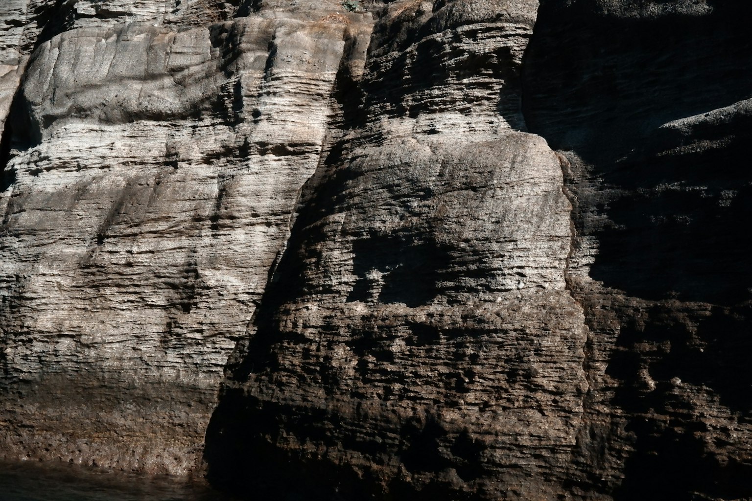 Scogliera di roccia stratificata con tonalità scure e motivi testurizzati