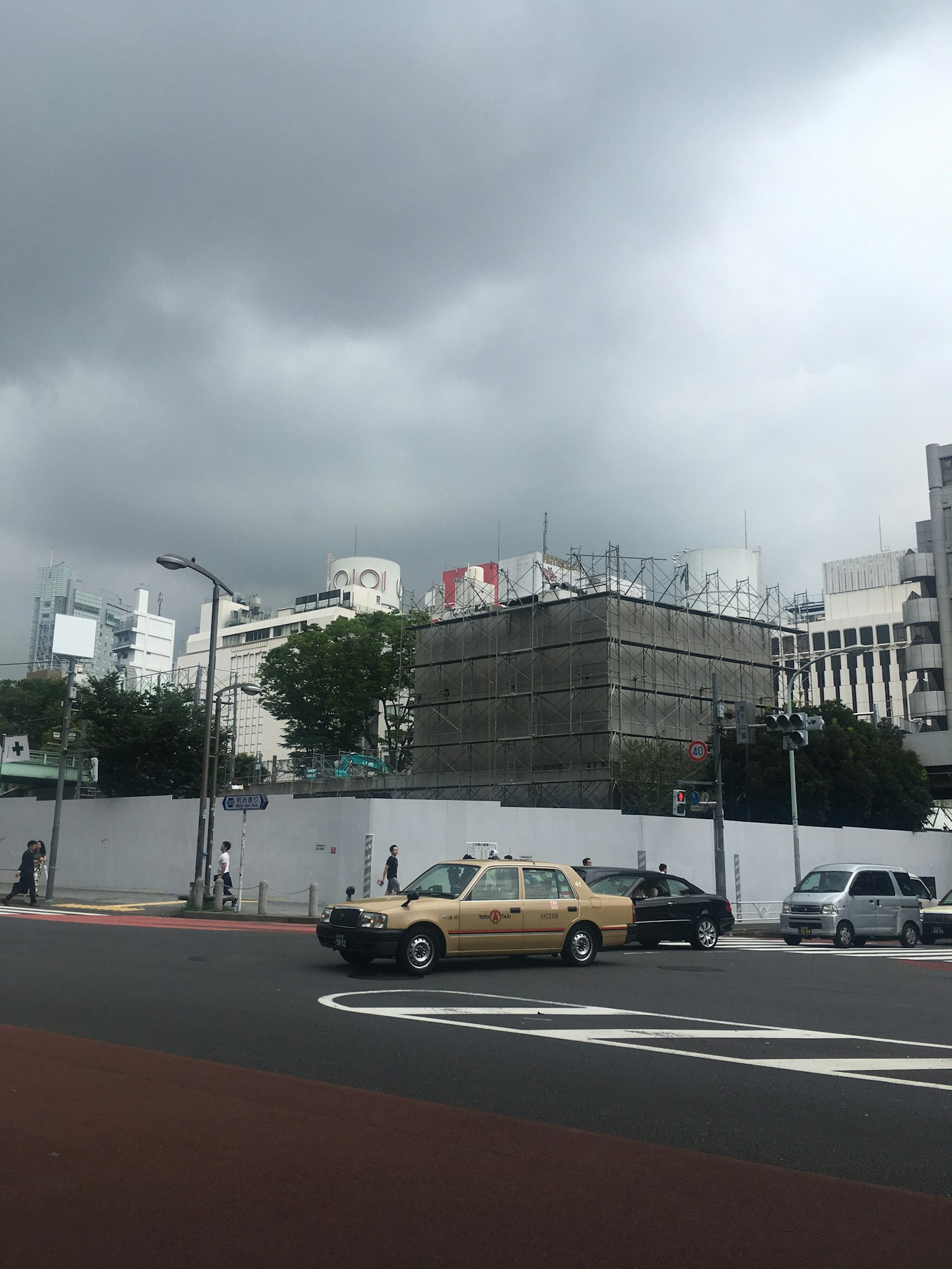Urban landscape under cloudy sky featuring a yellow taxi and a construction site
