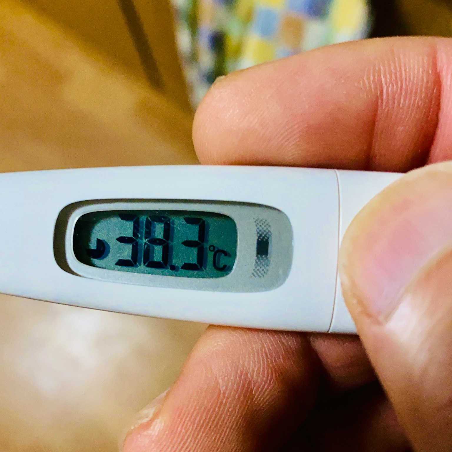 Main tenant un thermomètre affichant une température de 38,3 degrés Celsius