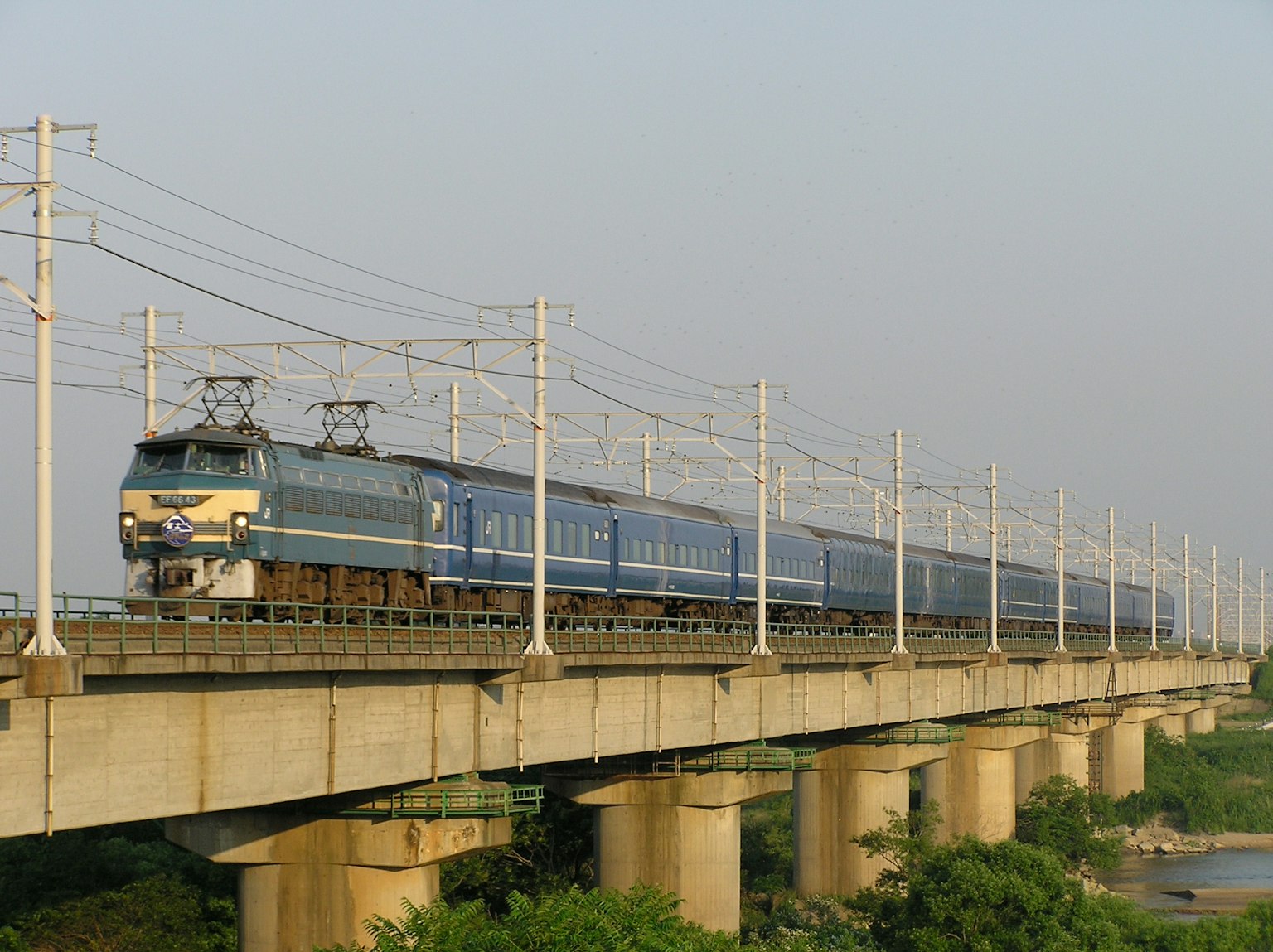 Blue train running on a bridge with power lines