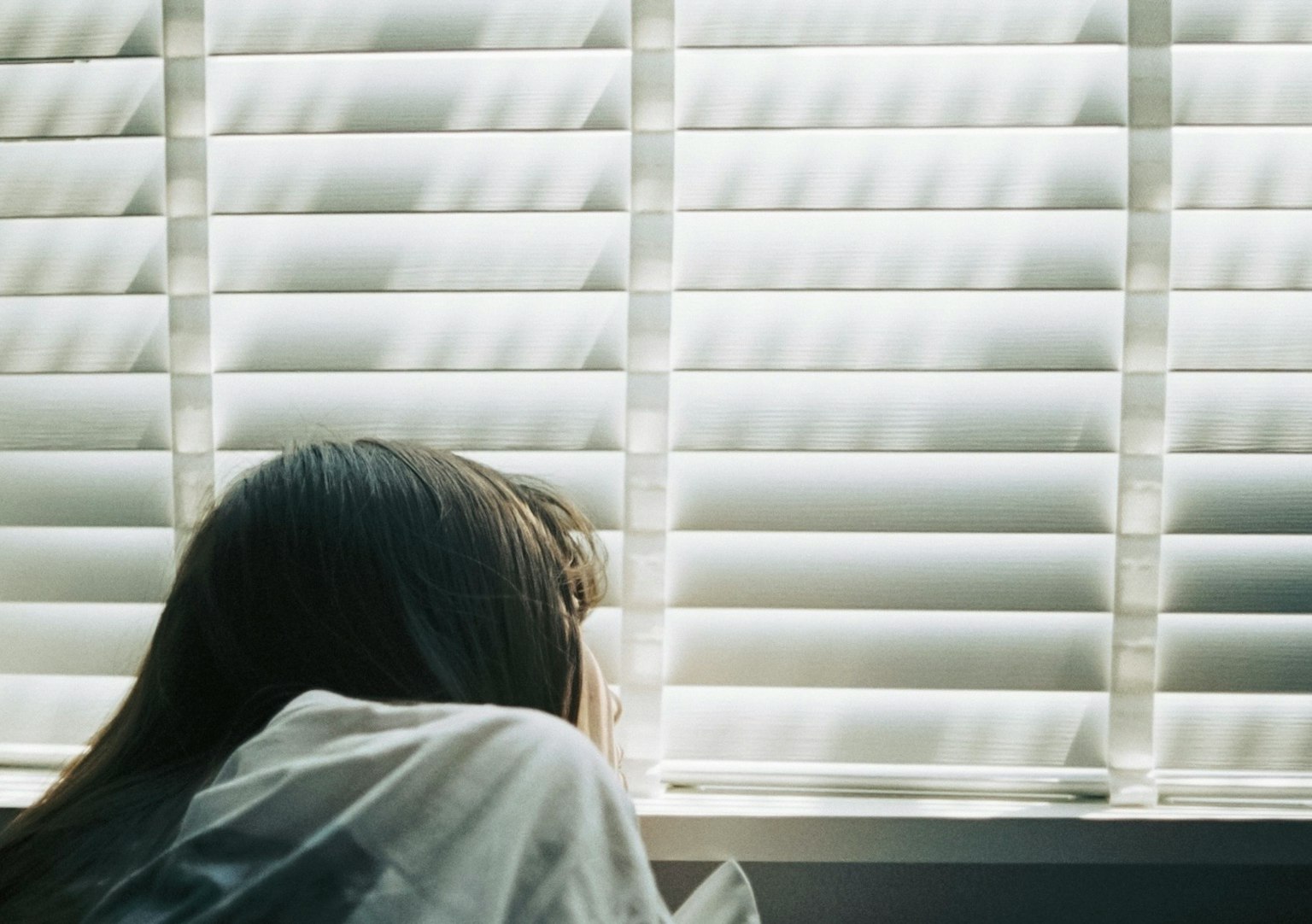 Una mujer mirando a través de las persianas con luz entrando