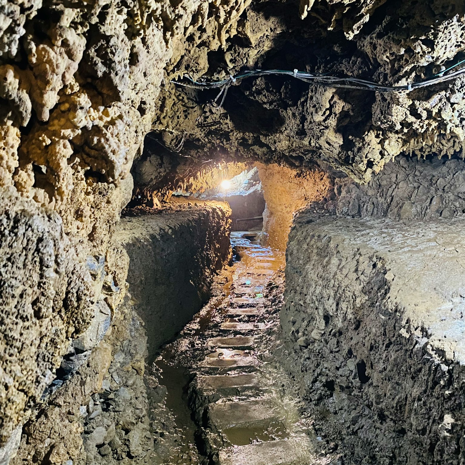 Interior of a narrow cave tunnel with a stone path along a wet ground