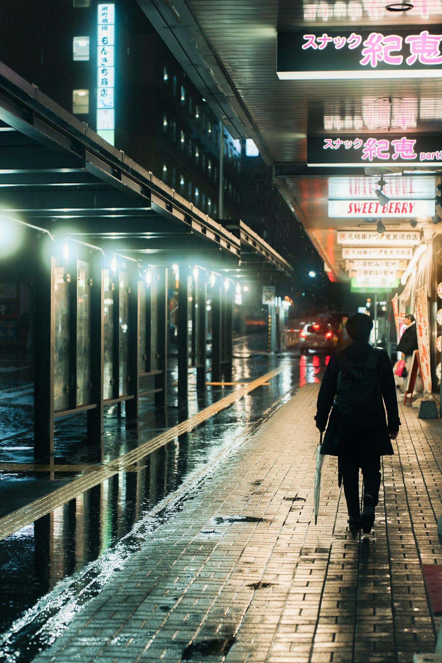 雨中打著傘的人走在霓虹燈下