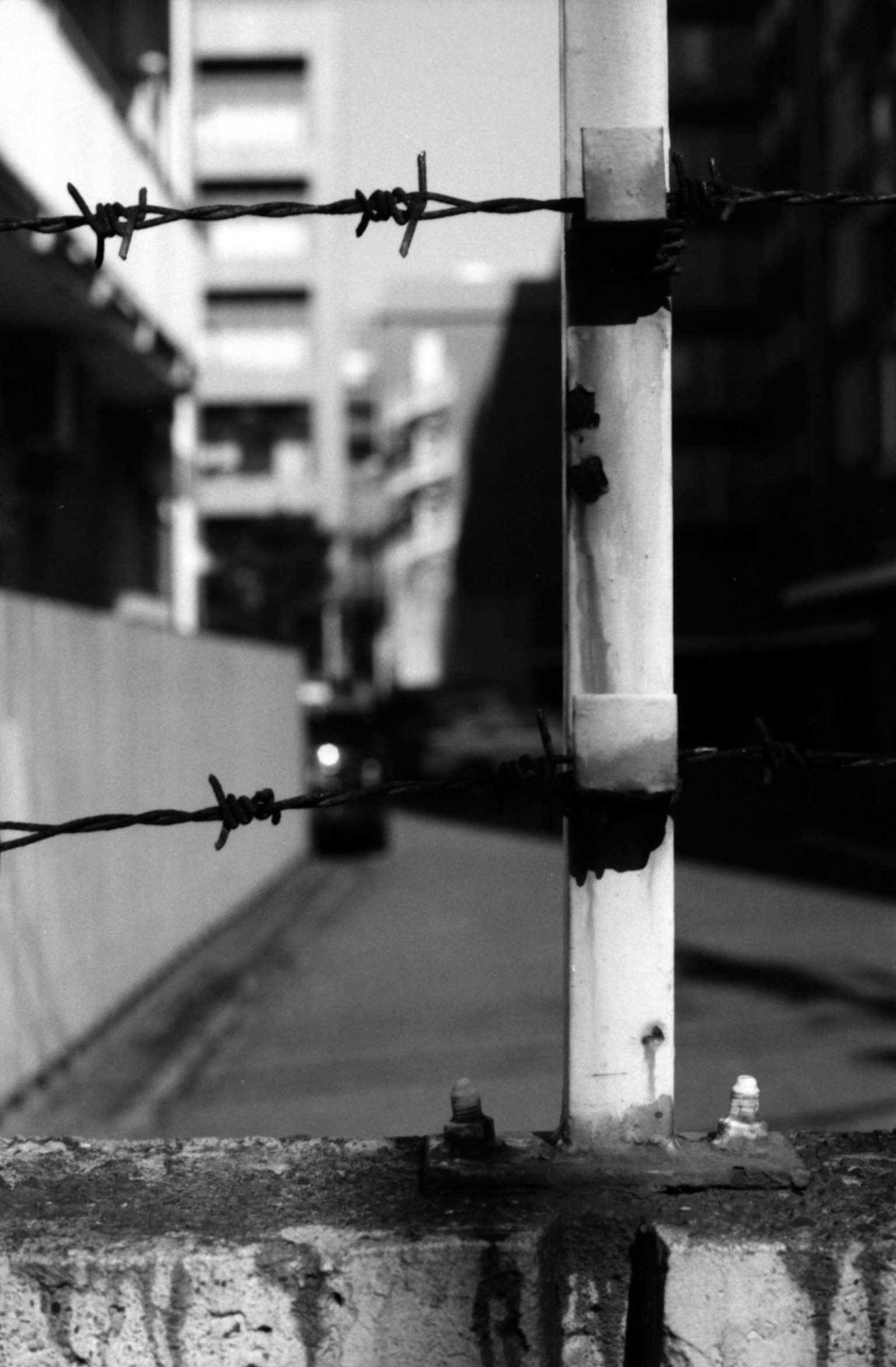 Close-up of barbed wire and concrete barrier with urban backdrop