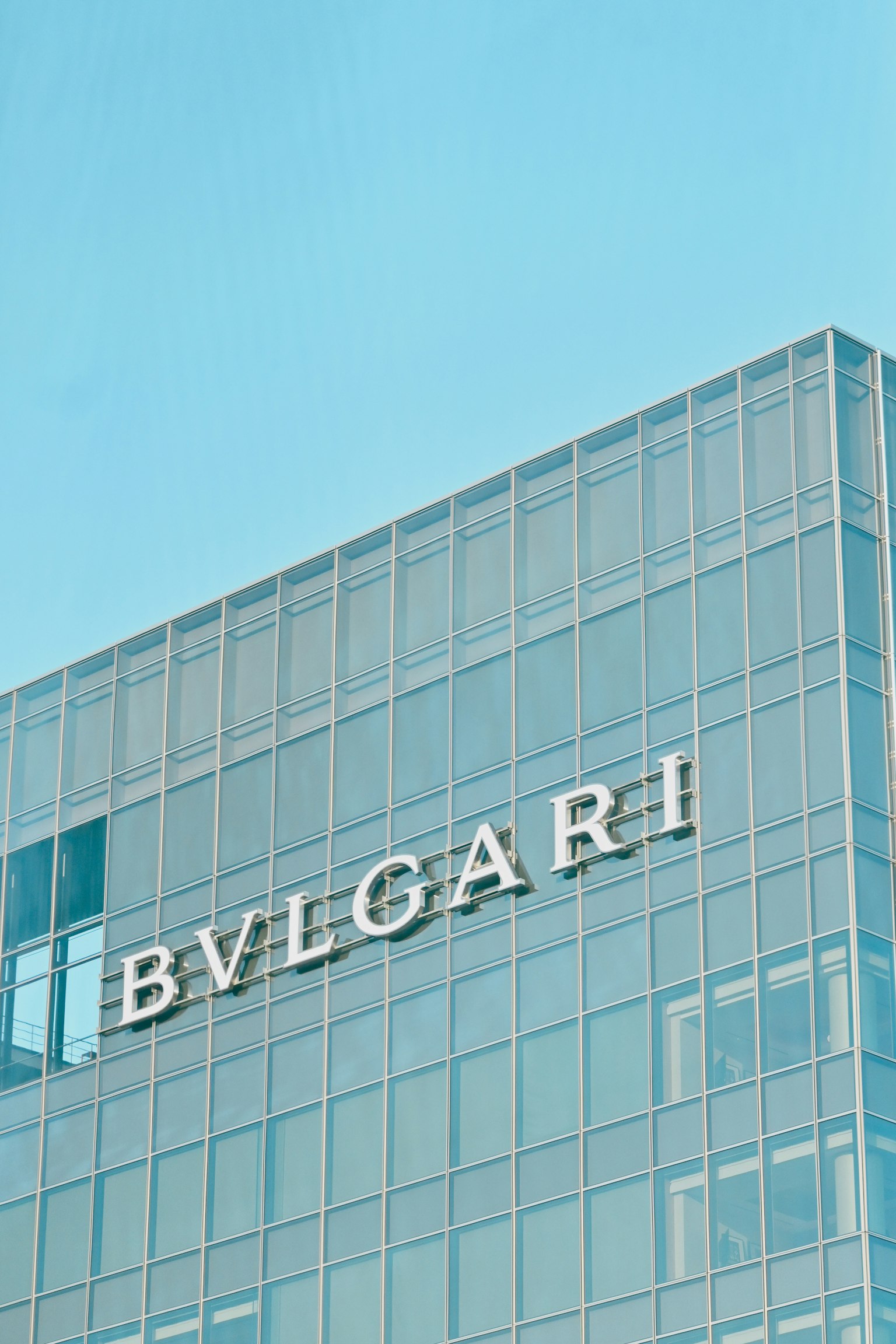 Glass building featuring Bvlgari logo under a clear blue sky
