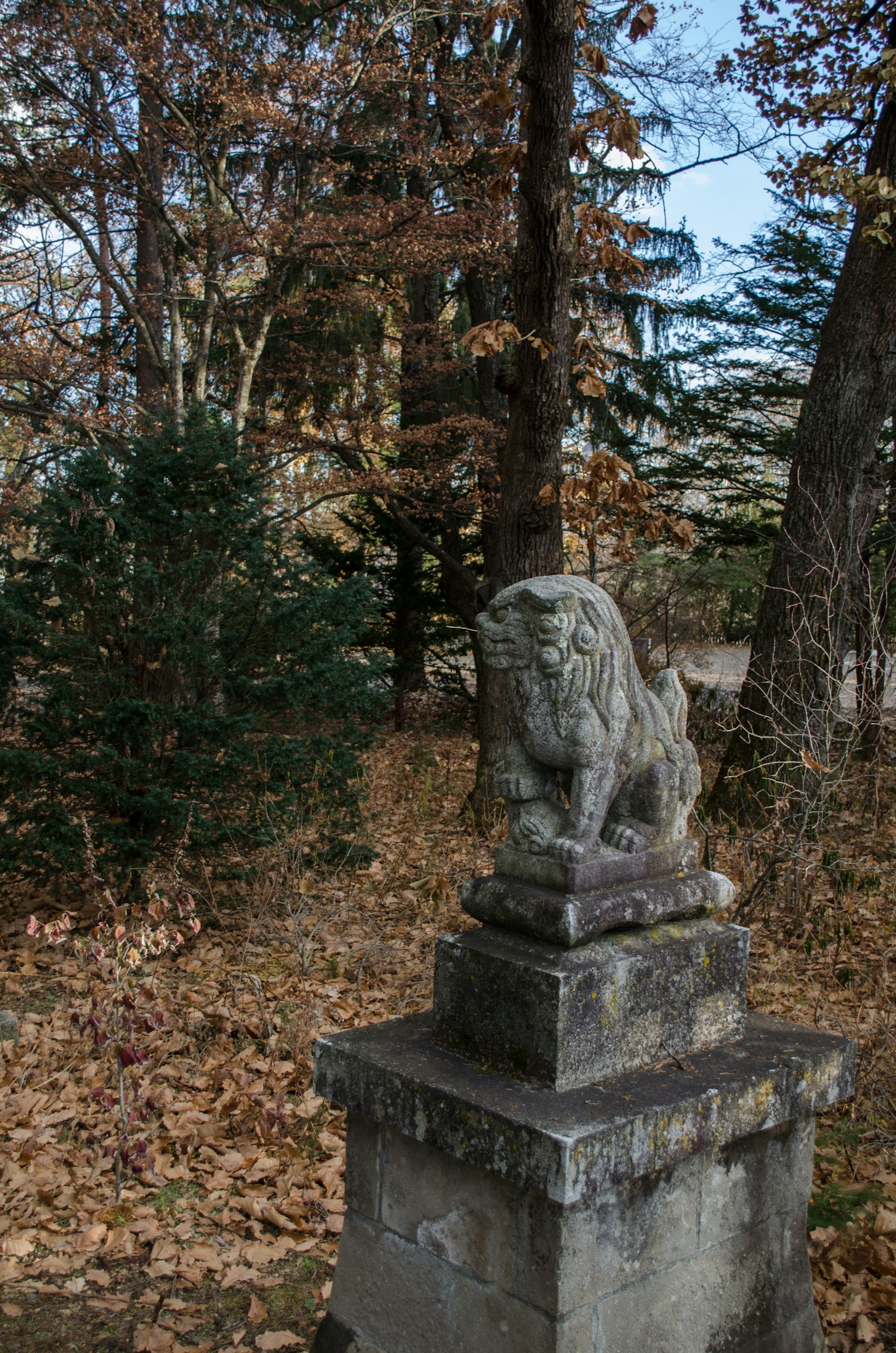 Une ancienne statue de lion en pierre se dresse dans un paysage entouré d'arbres et de feuilles tombées