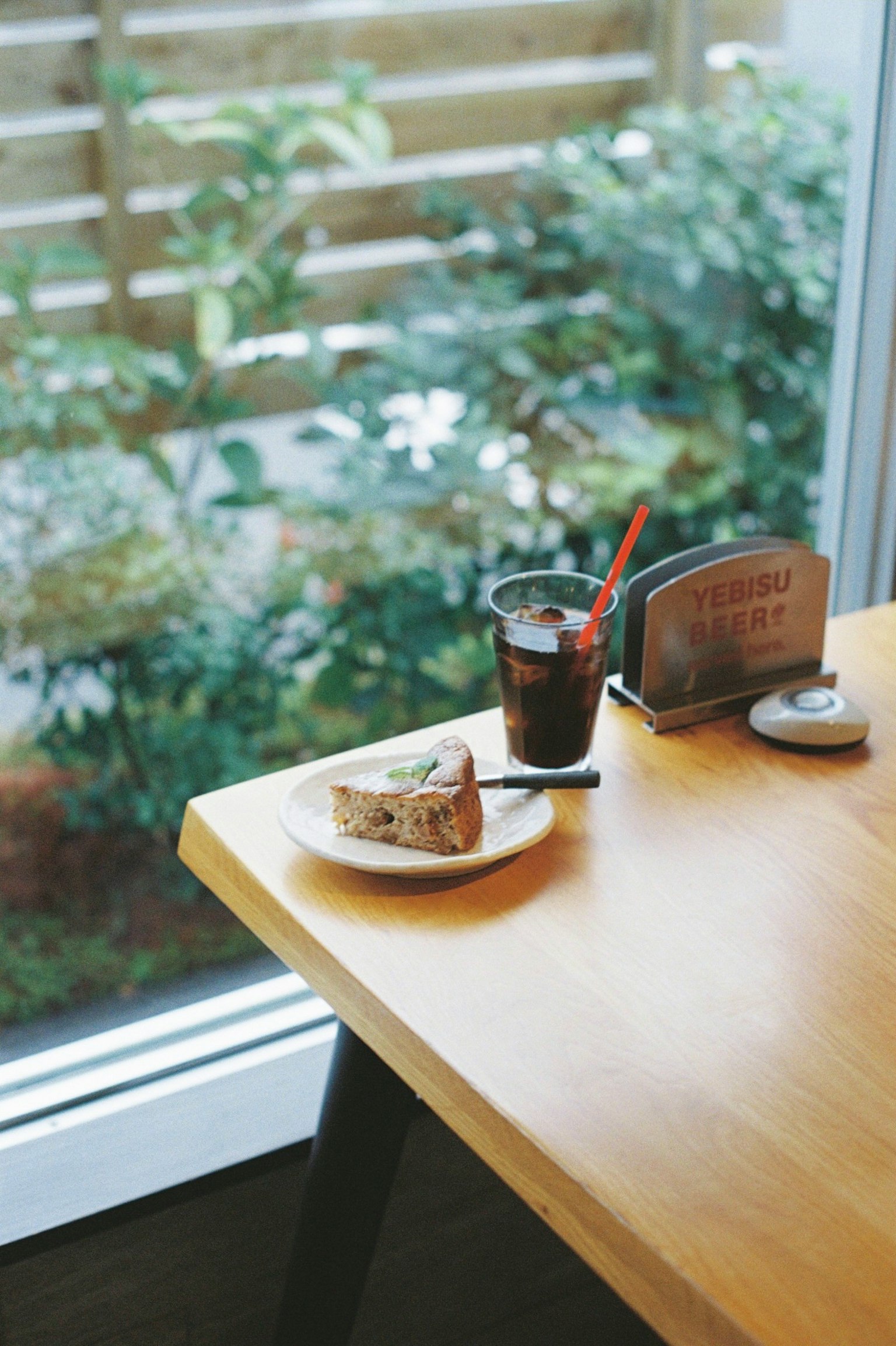 Ein Foto von einem Kuchen und einem Getränk auf einem Tisch mit Grünpflanzen, die draußen sichtbar sind