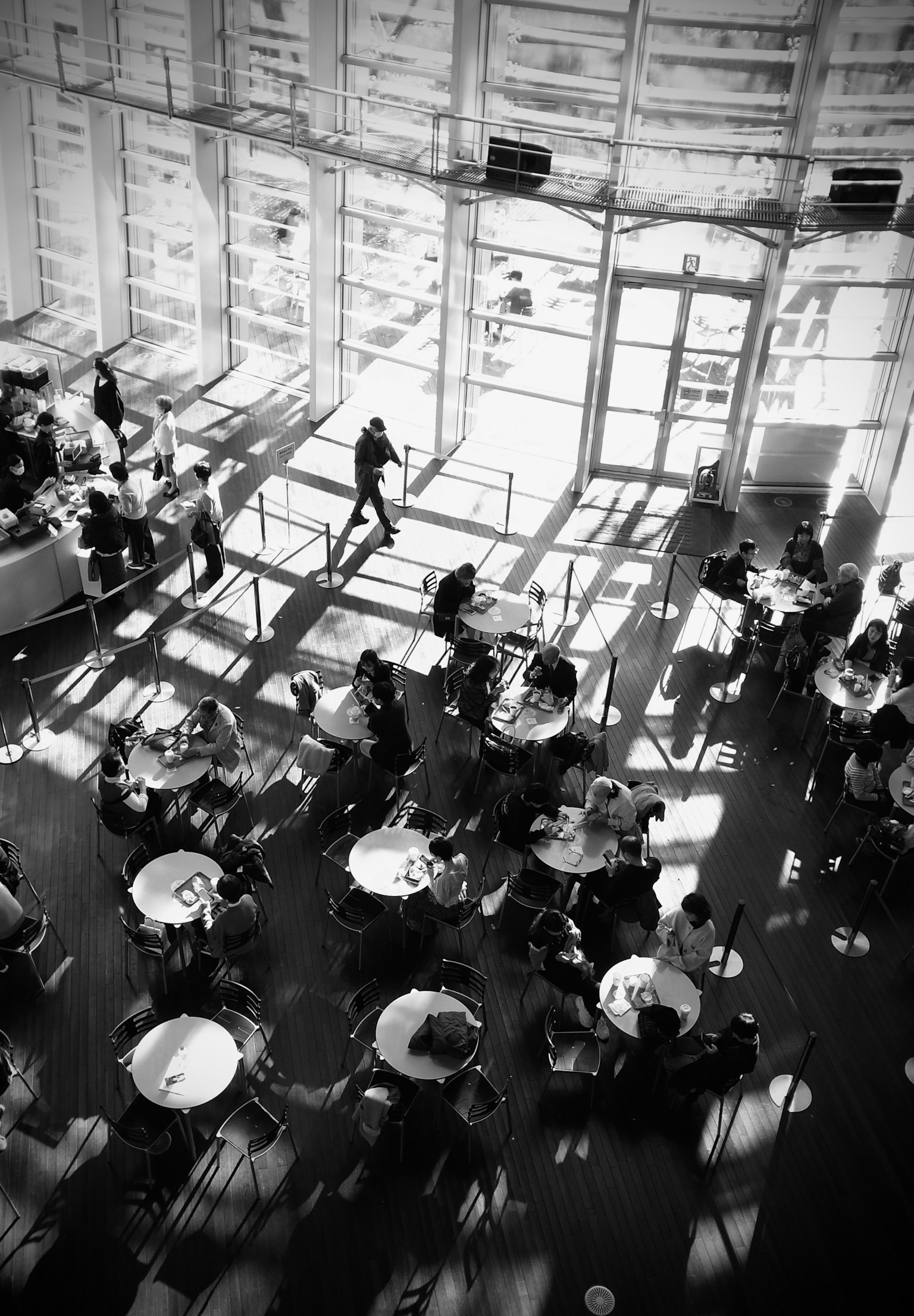 Vista aerea in bianco e nero di un interno di caffè con numerosi tavoli e sedie e ombre suggestive create dalla luce naturale