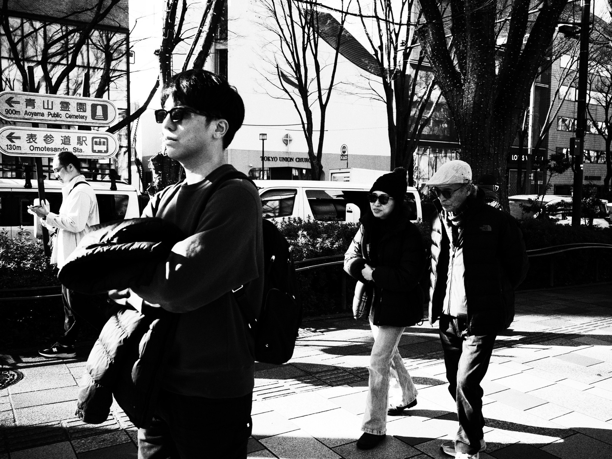 街中を歩く人々のモノクロ写真 若い男性が腕を組み その後ろに他の人々が歩いている