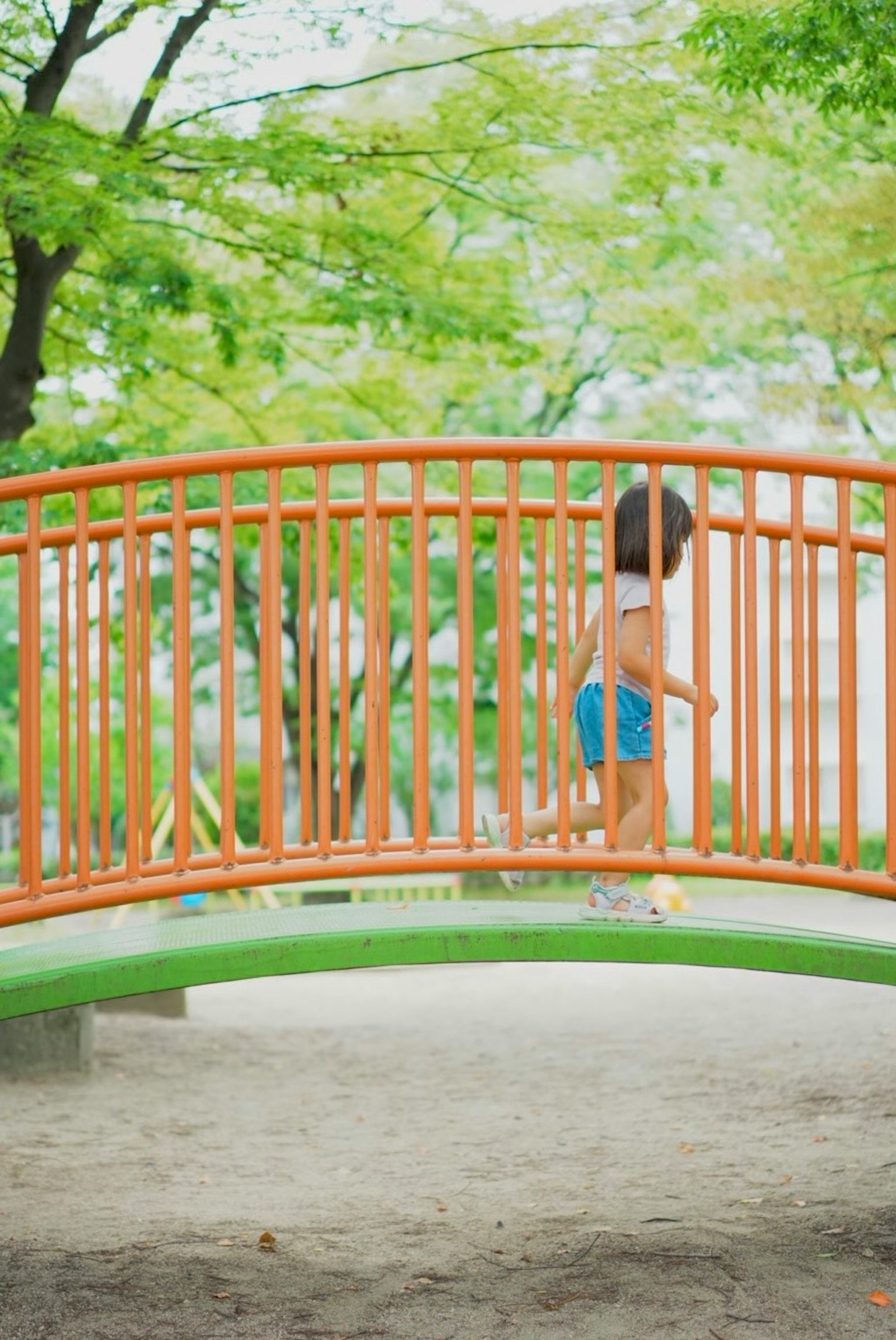 孩子在公园里走在橙色的桥上，周围是绿色的树木