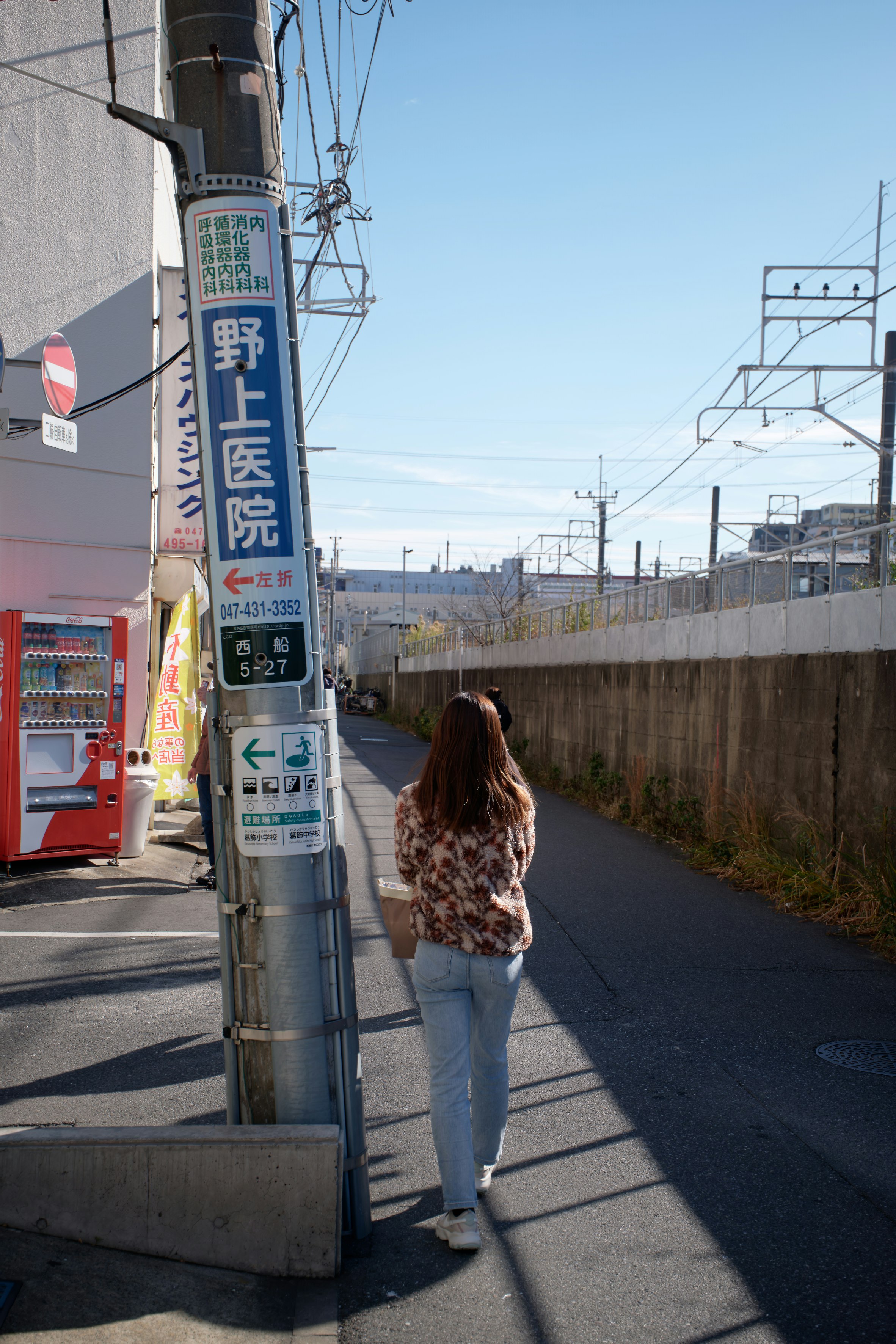 傾いた電柱の看板と人物が並ぶ路地のスナップ