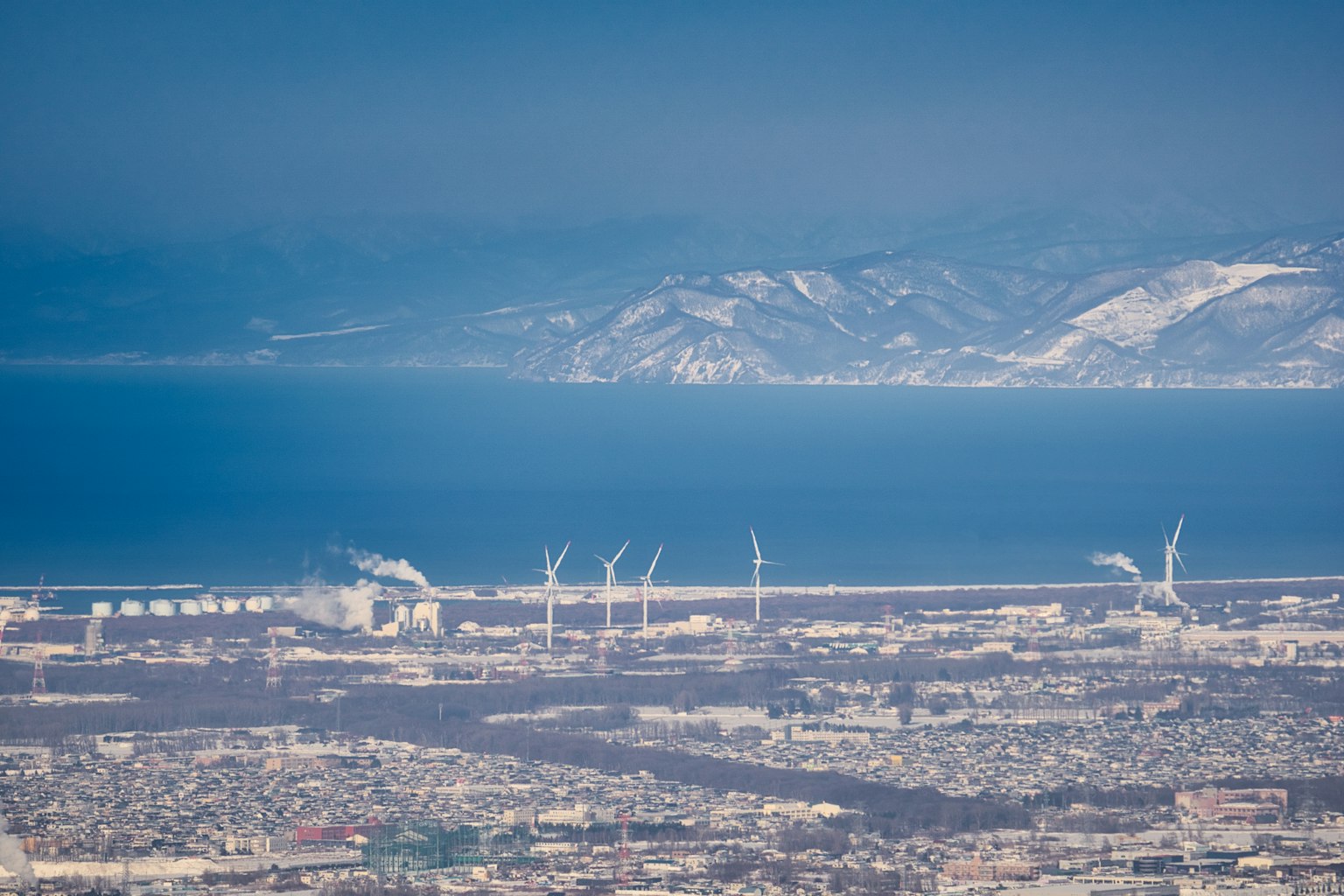 Vista aerea di una città costiera con turbine eoliche e oceano blu