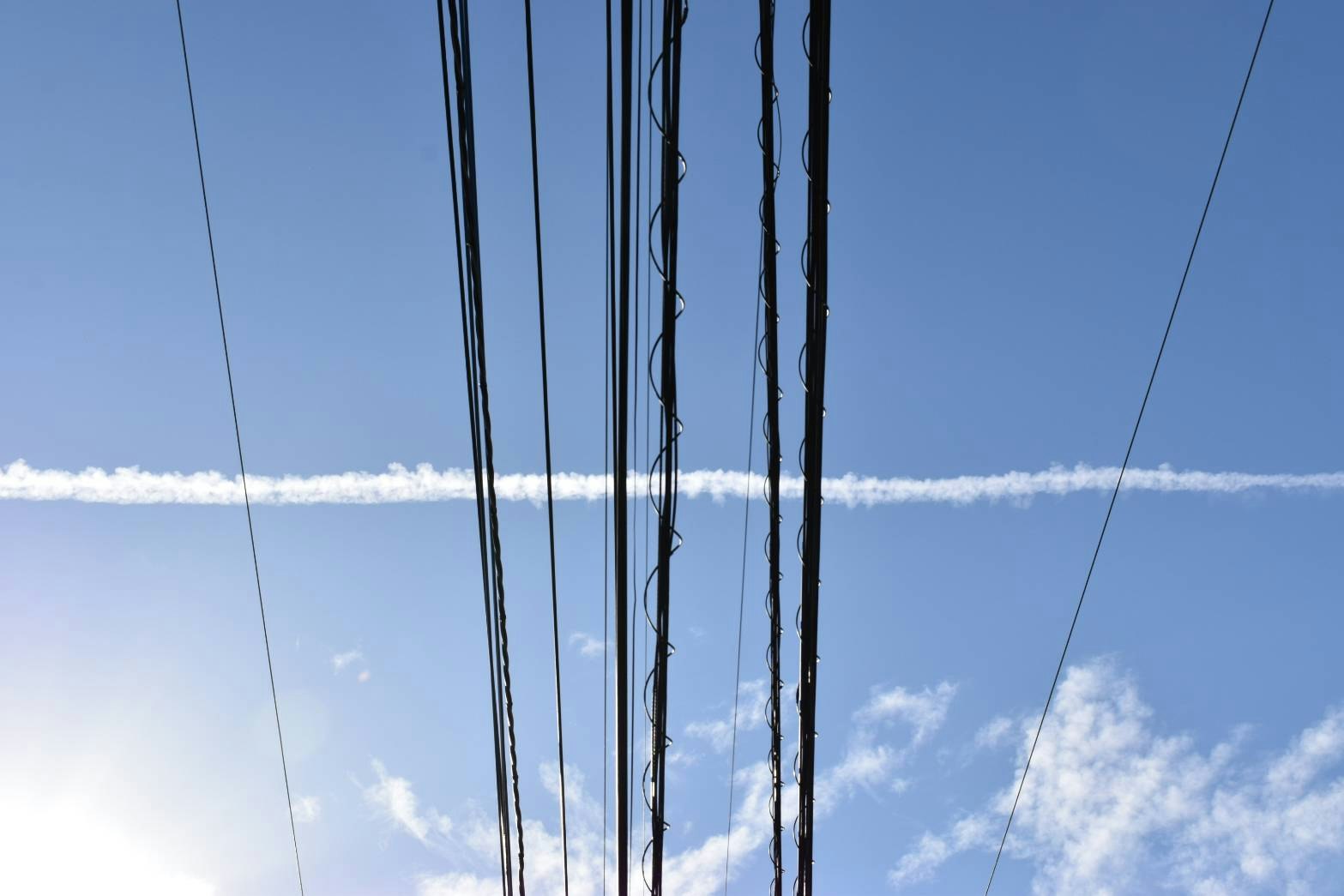 青空の下、電線と飛行機雲が交差する空の風景