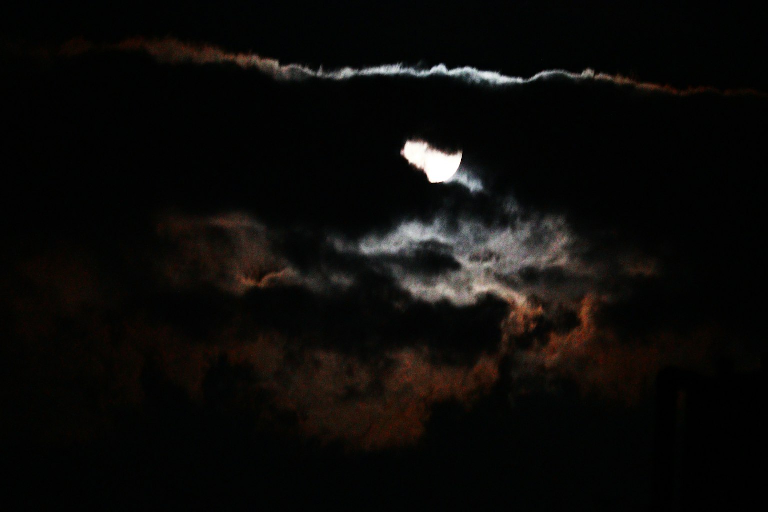 Mysteriöser Nachthimmel mit dem Mond, der durch dunkle Wolken blitzt