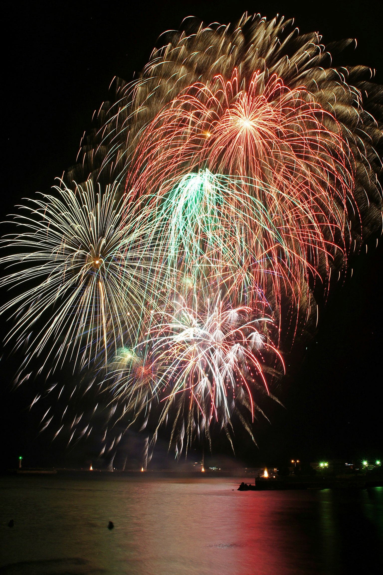 Colorful fireworks bursting in the night sky reflecting over the sea