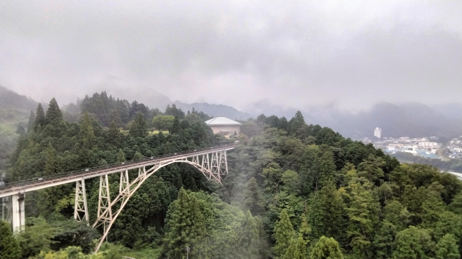 Bogenbrücke über grüne Berge, die im Nebel gehüllt sind