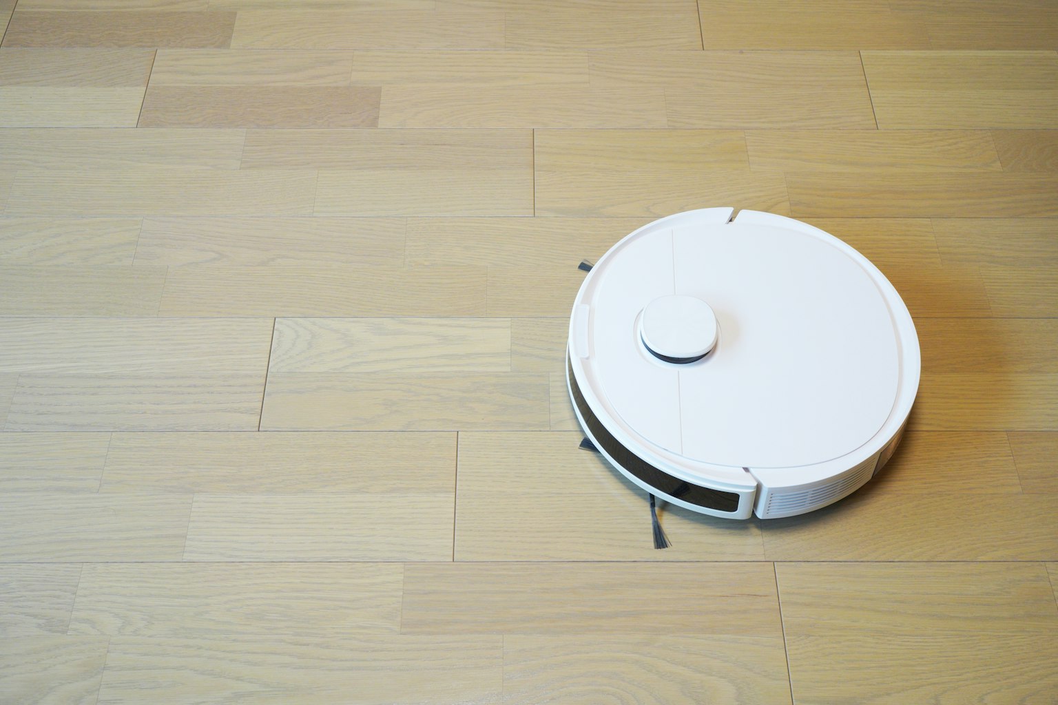 Un aspirateur robot blanc se déplaçant sur un sol en bois
