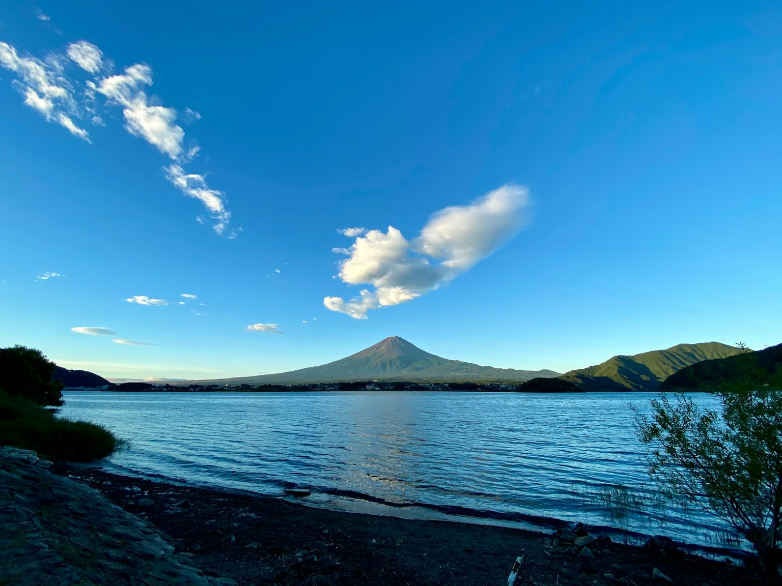 Vista panoramica di un lago e una montagna, cielo blu con nuvole bianche, superficie d'acqua calma