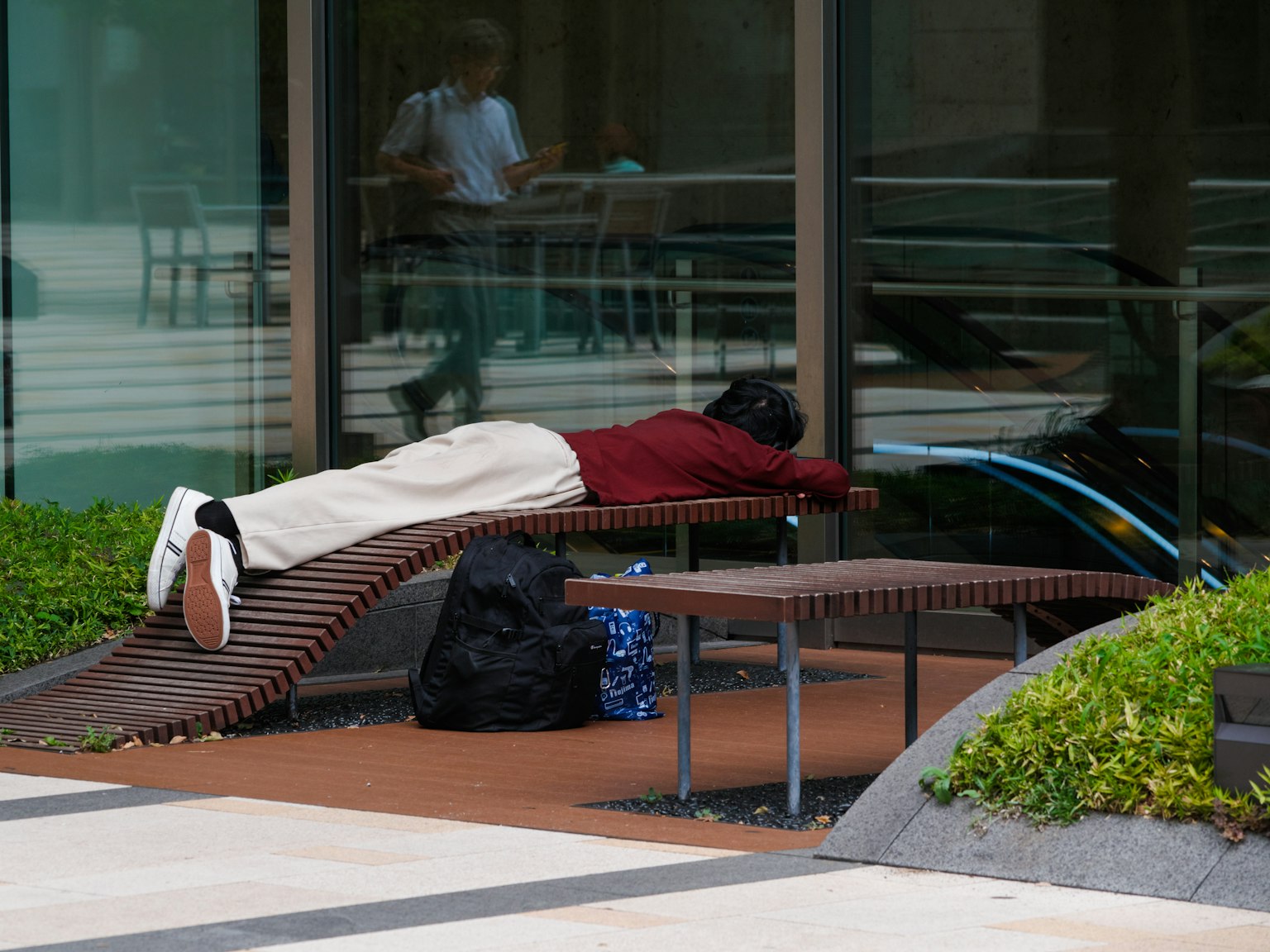 Persona sdraiata a faccia in giù su una panchina con piante verdi nelle vicinanze