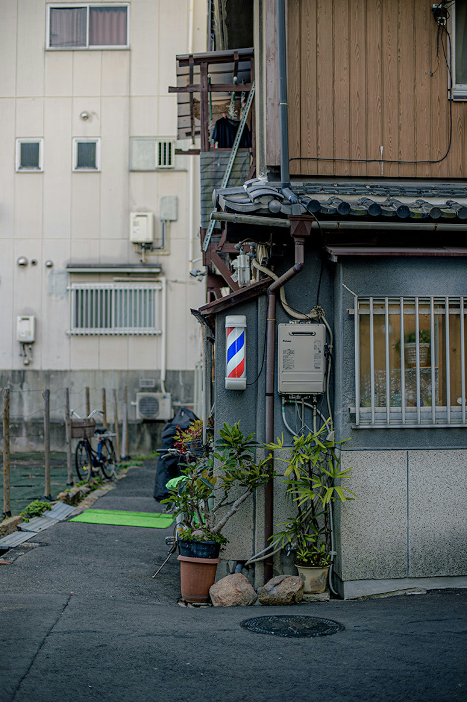 Exterior of a barbershop in a narrow alley featuring a green path and plants