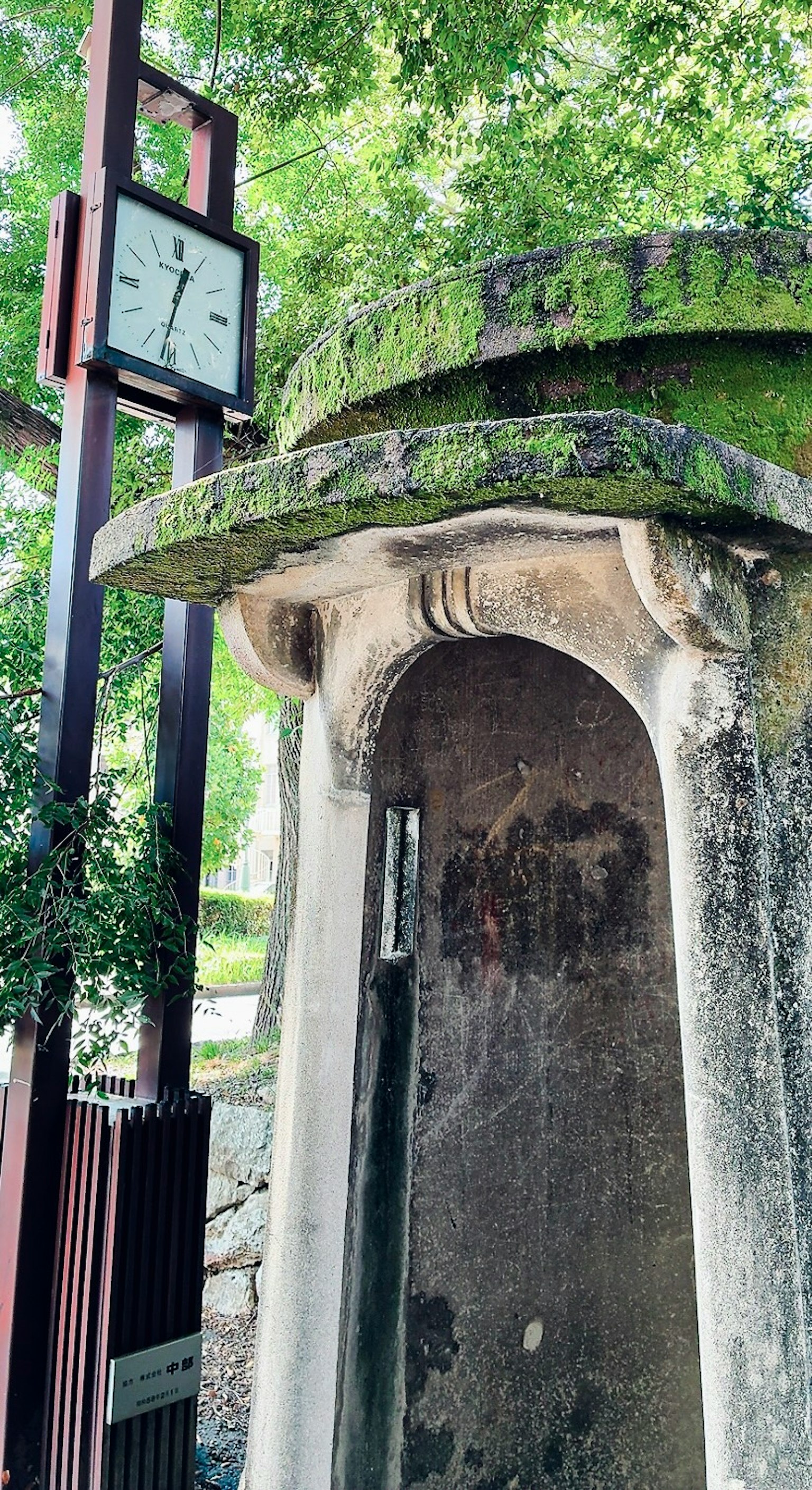 古い石造りの小屋と現代的な時計が並ぶ風景 緑に覆われた周囲