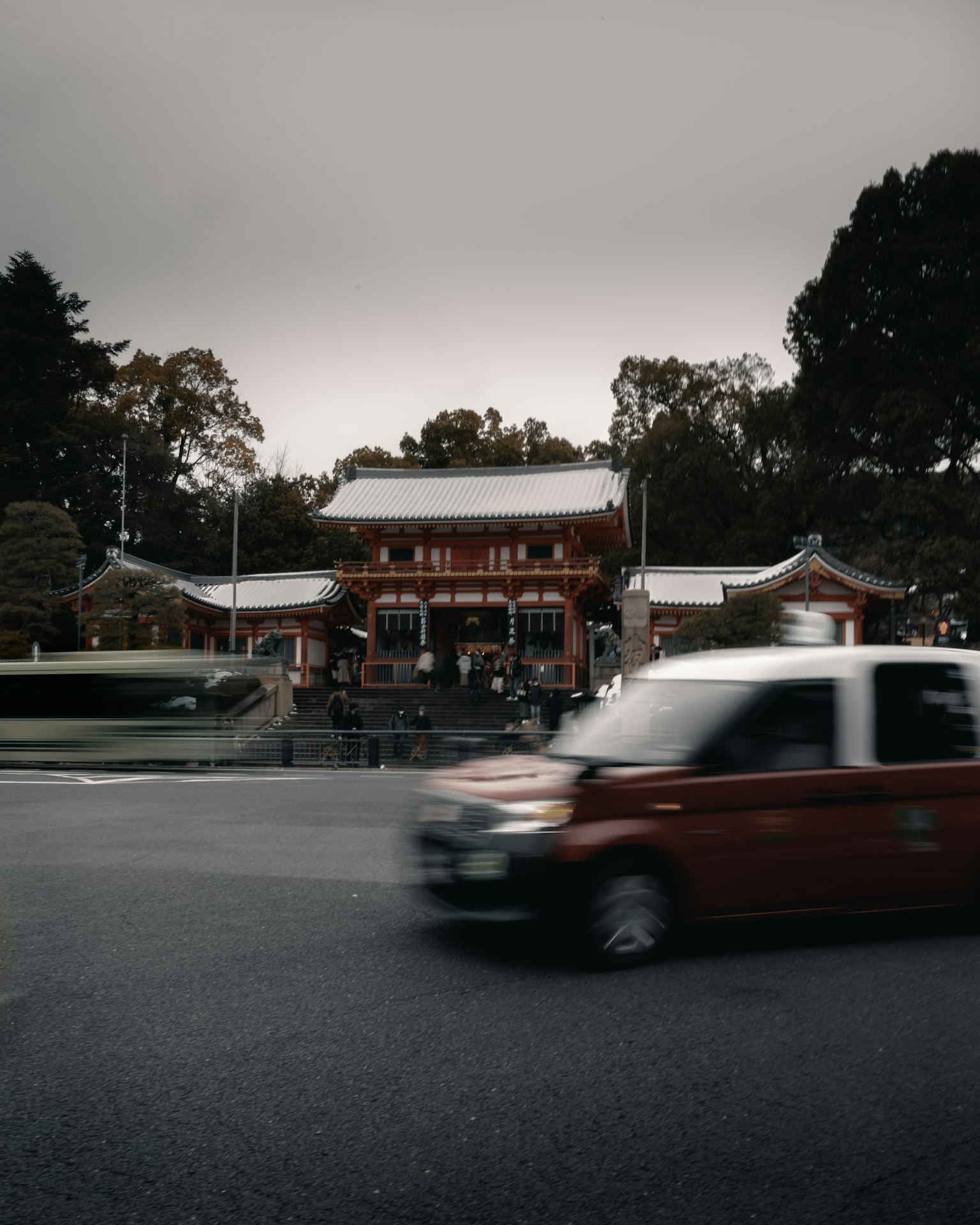 Traditional Japanese shrine under a dark sky with a red car in motion