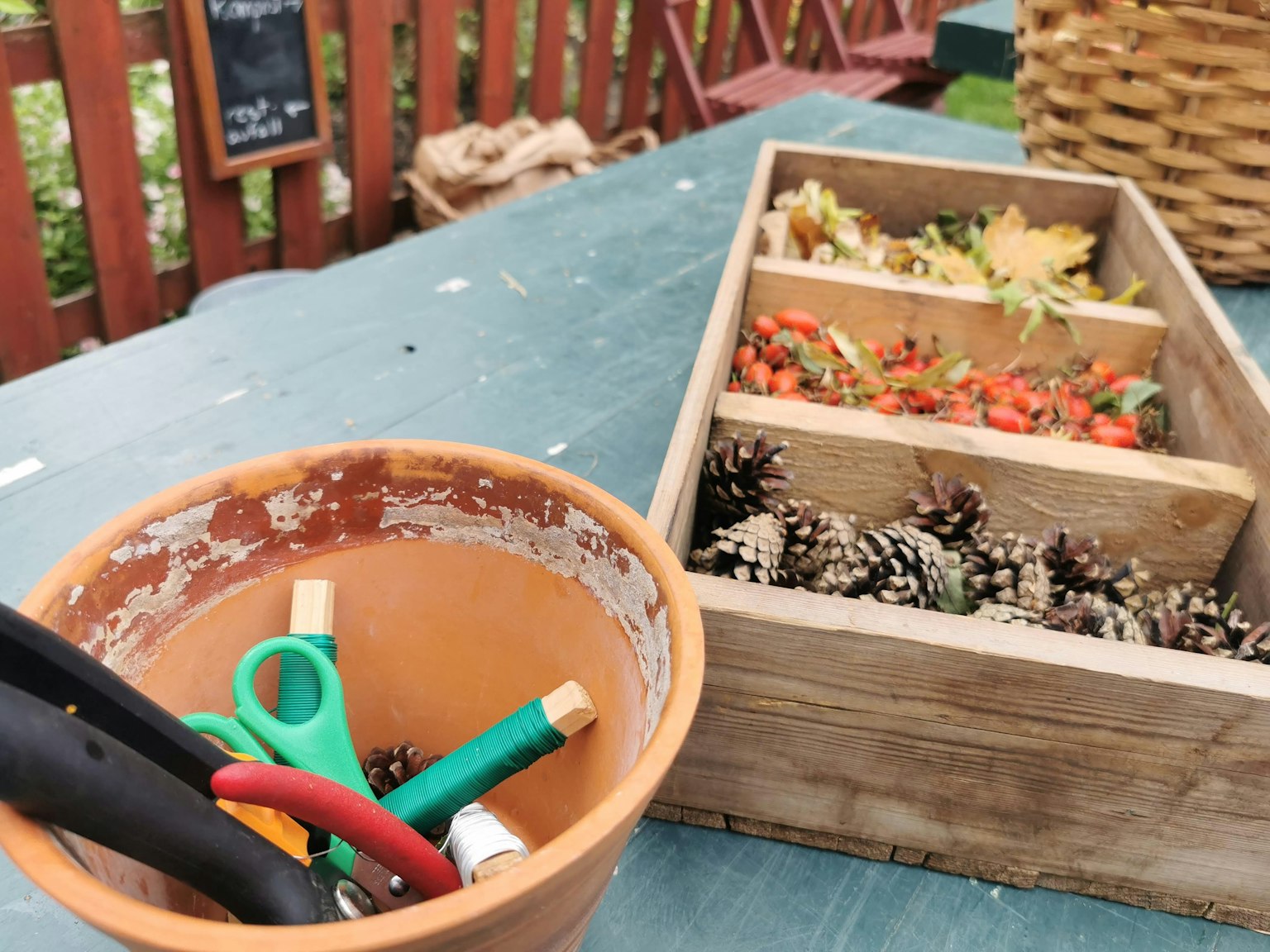 Gardening tools in a terracotta pot and a wooden box with plant materials