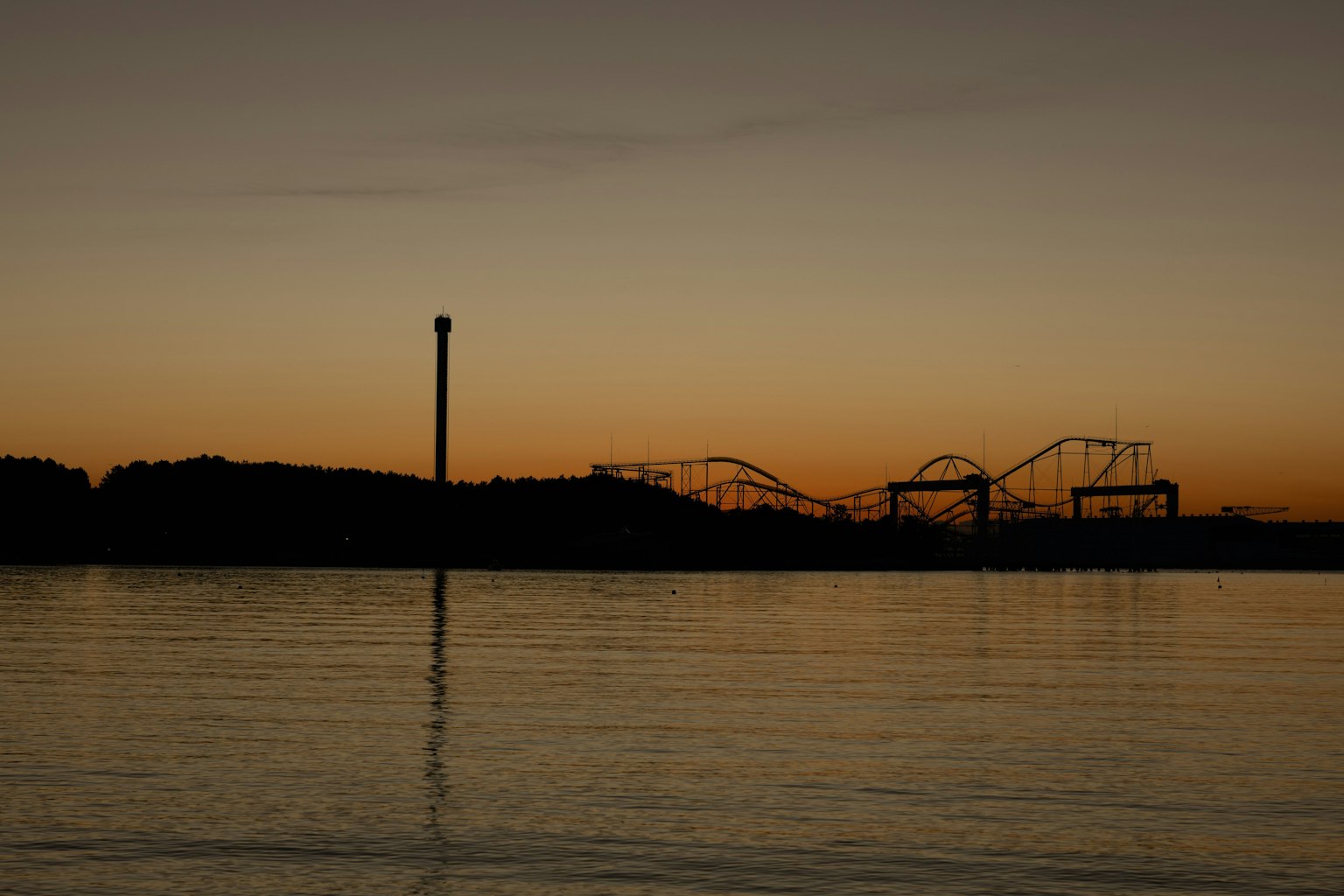 Silhouette d'un parc d'attractions au crépuscule avec réflexion sur l'eau