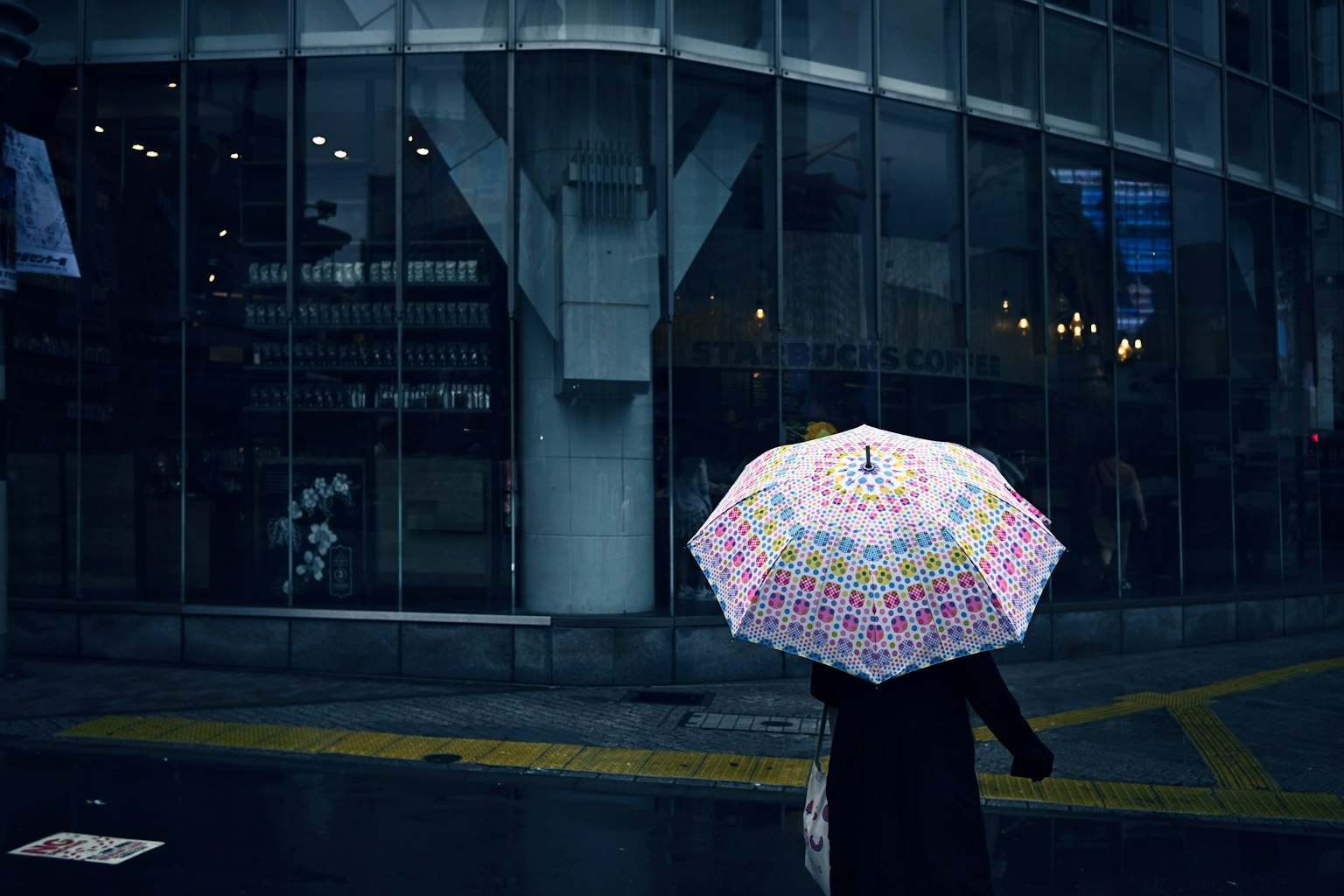 一个人在雨天的城市里走，手里拿着五彩缤纷的雨伞