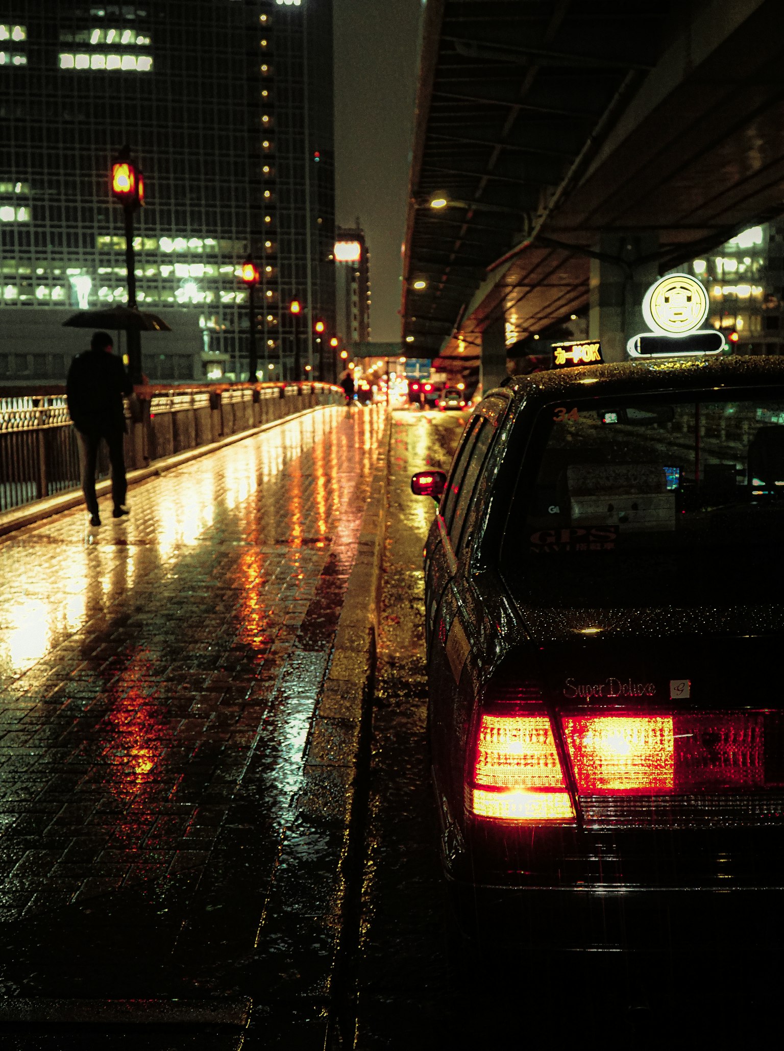 Cảnh thành phố ban đêm với vỉa hè ướt mưa và taxi sáng đèn