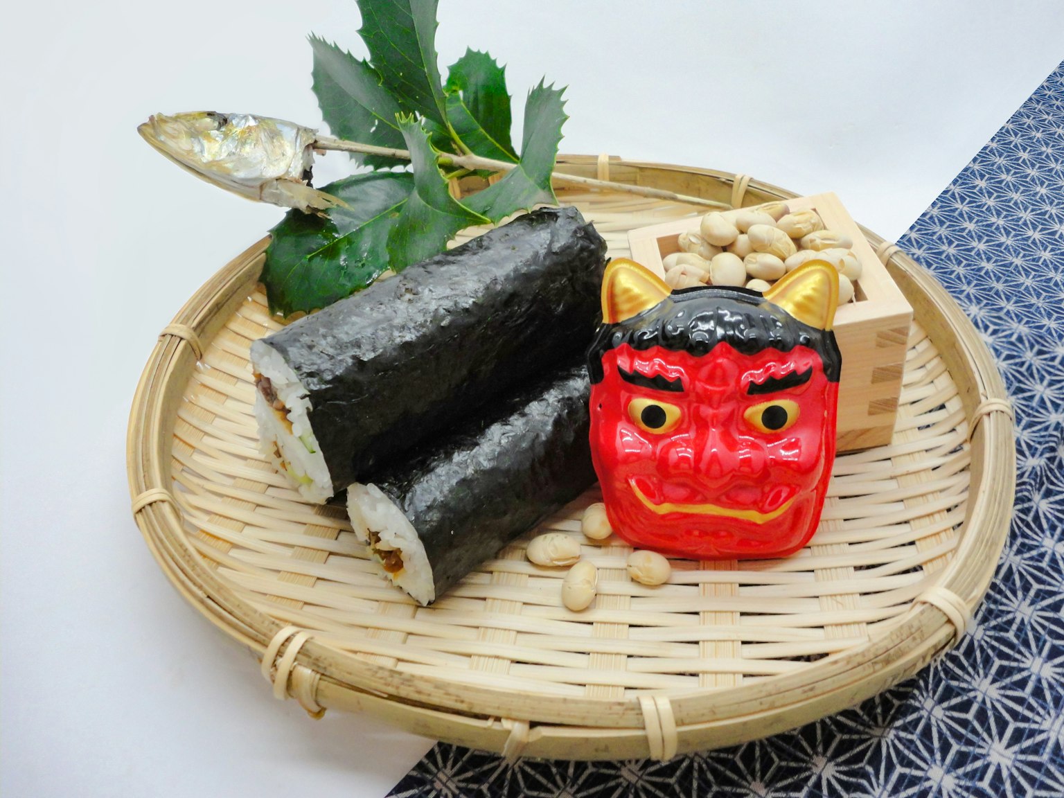 Un plato de bambú con rollos de sushi y una decoración de demonio rojo con frijoles y hojas que muestran la cocina japonesa tradicional