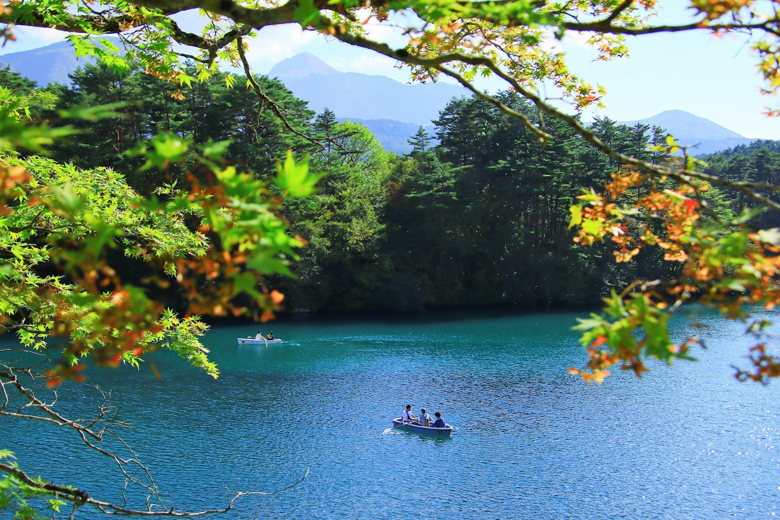 Sebuah danau biru tenang dikelilingi pegunungan dengan orang-orang berkanu