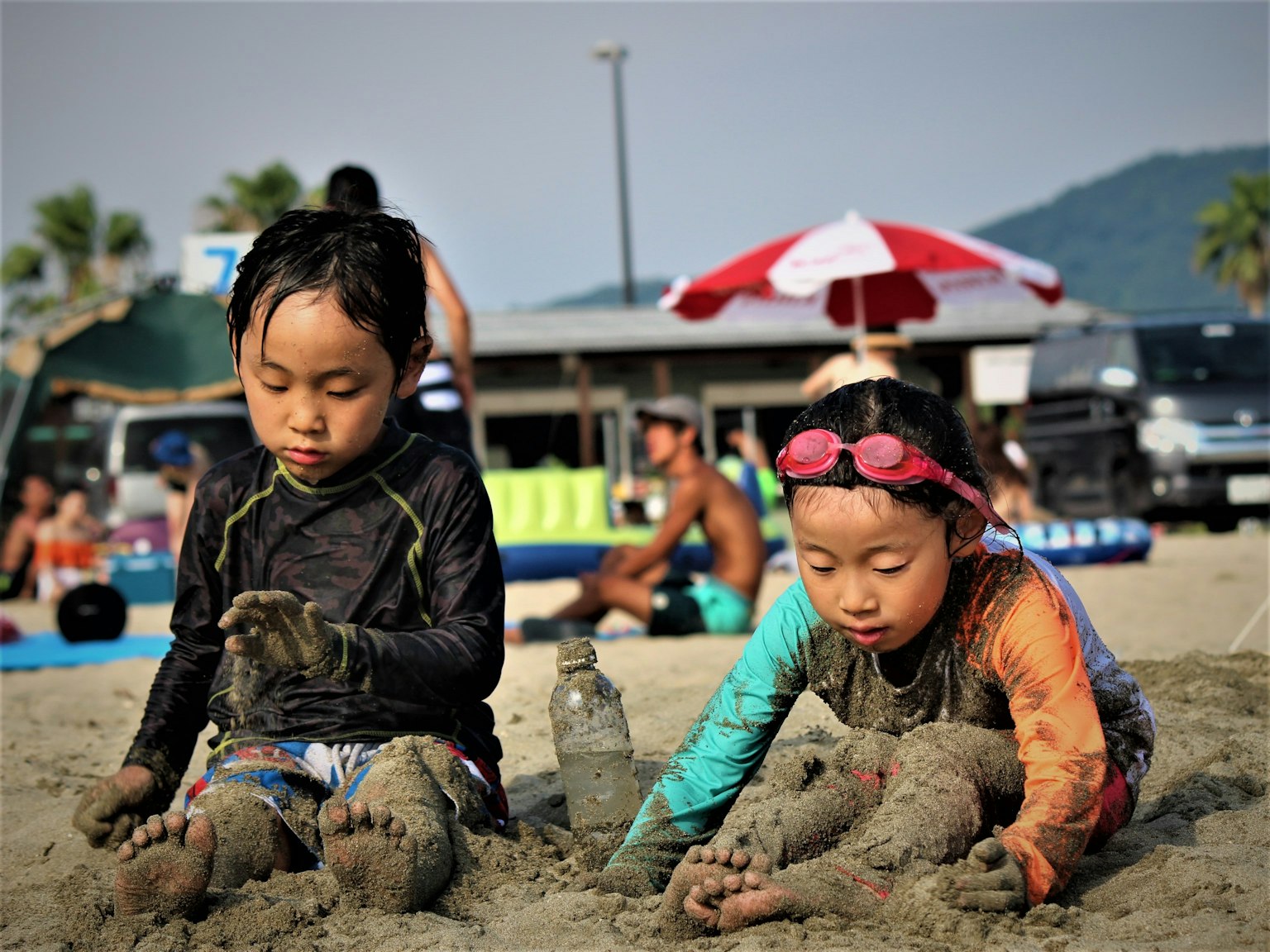 子供たちが砂浜で遊んでいる様子 海辺で砂遊びをする二人の子供 カラフルな水着を着ている