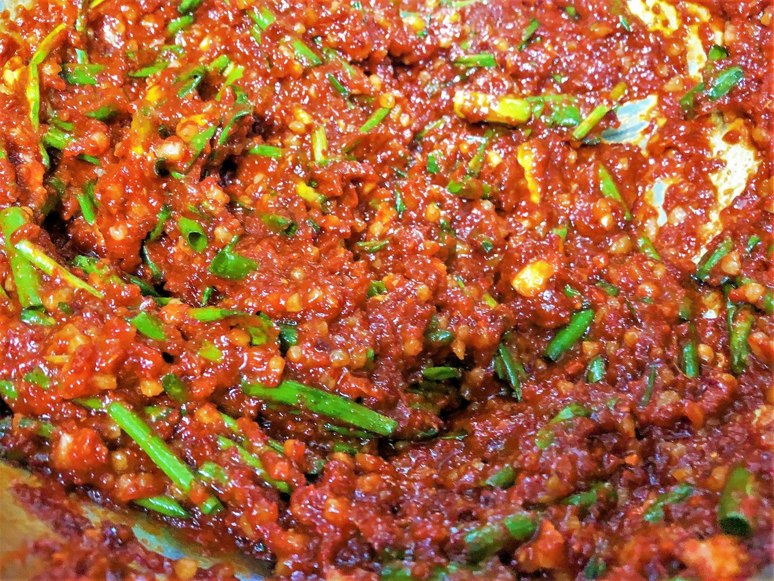 A mixture of red sauce and finely chopped green onions in a bowl