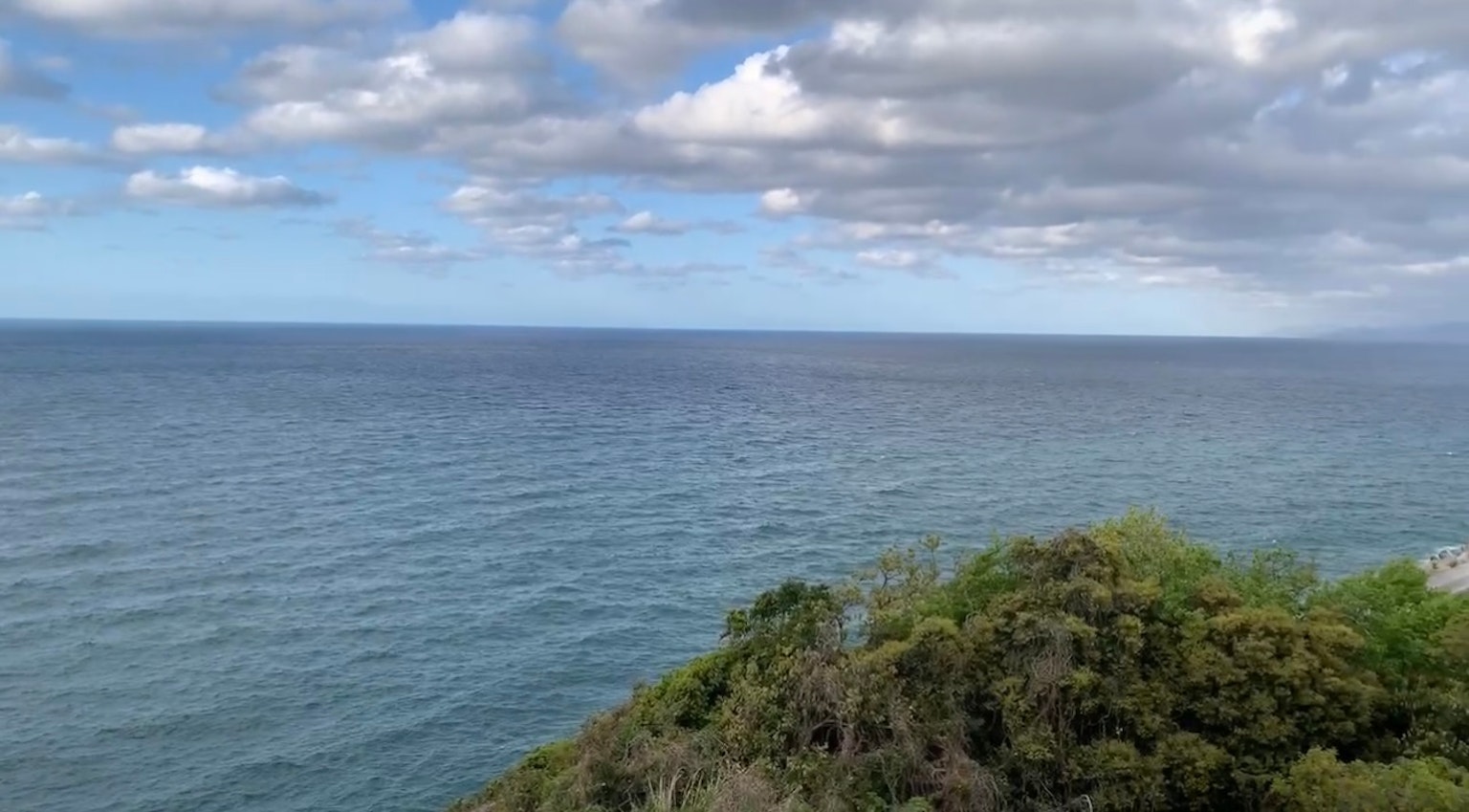 藍色海洋和多雲天空的風景，海岸線沿著綠色植被