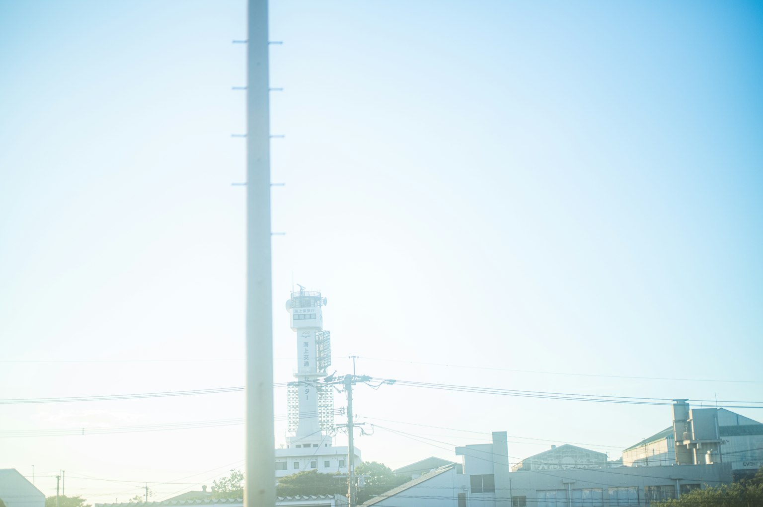 Ein hoher Strommast und ein Leuchtturm unter einem klaren blauen Himmel sichtbar