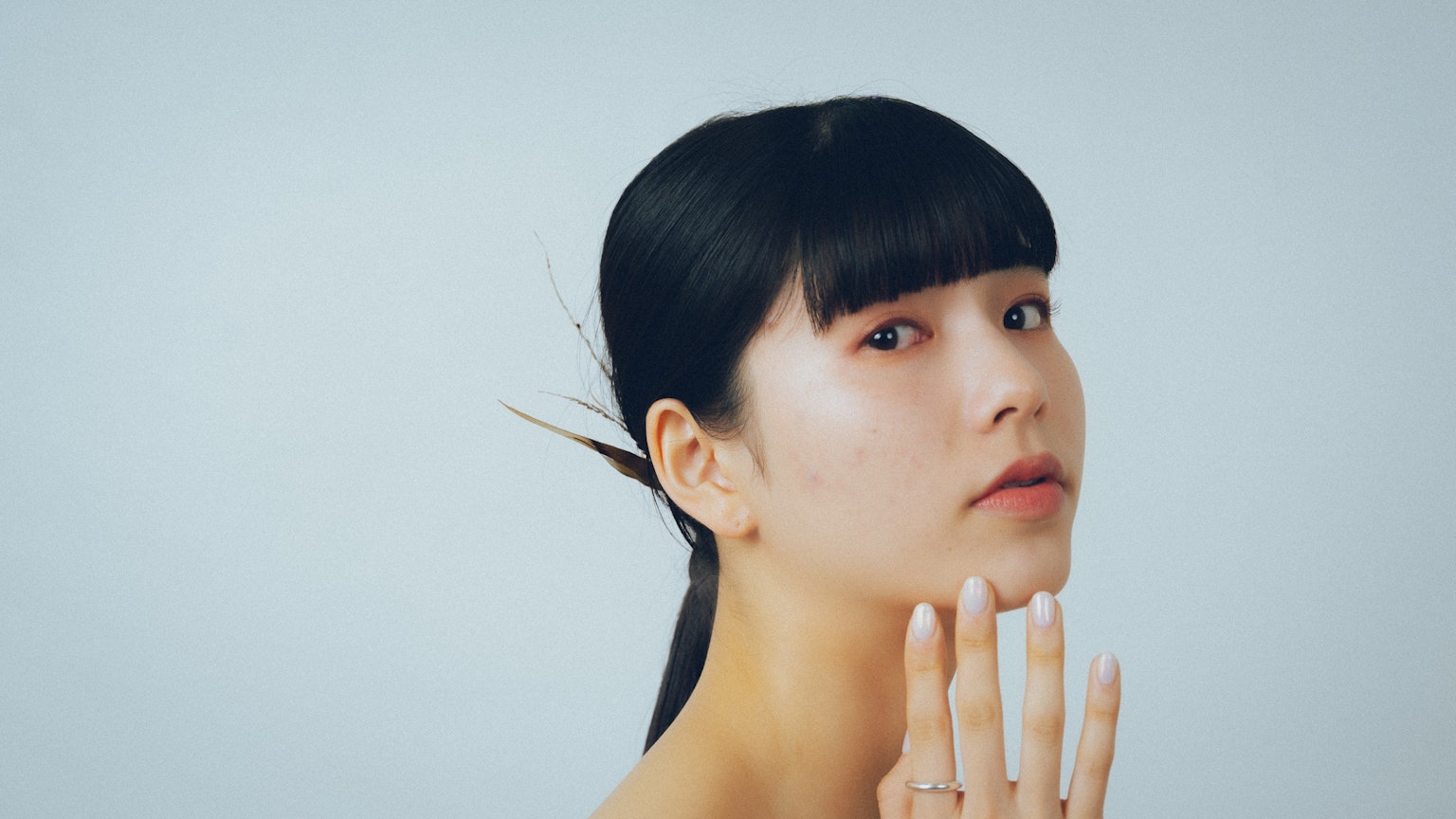 Portrait of a woman gently touching her face with a natural expression and simple background