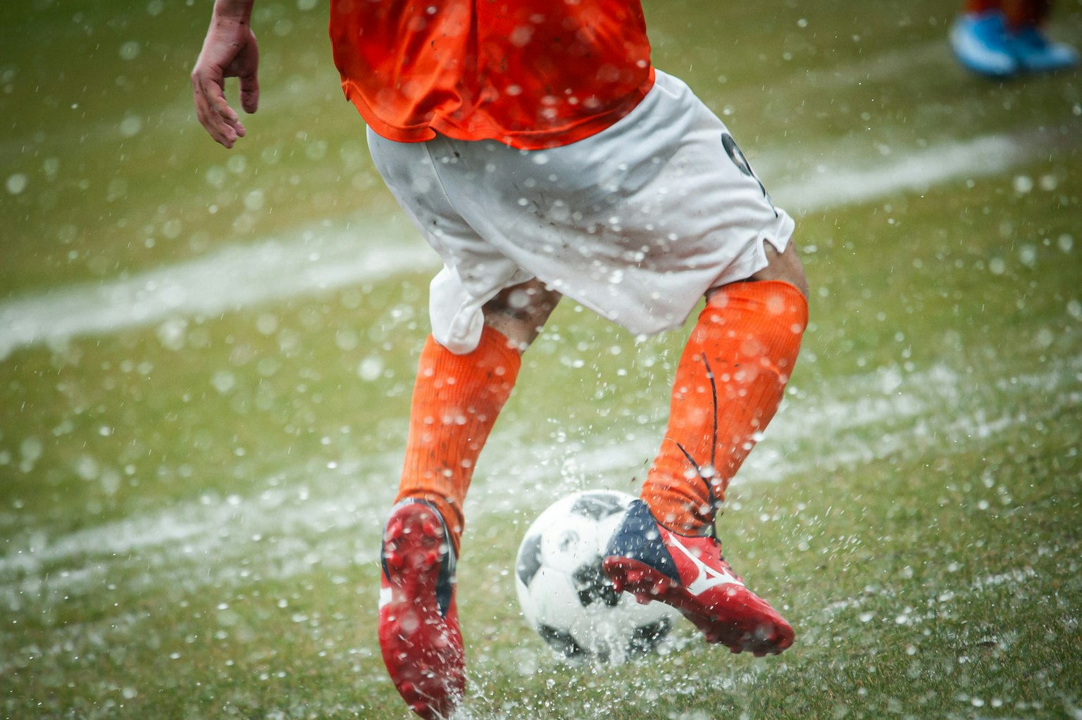 Un giocatore che calcia un pallone da calcio su erba bagnata indossando un'uniforme arancione e scarpe