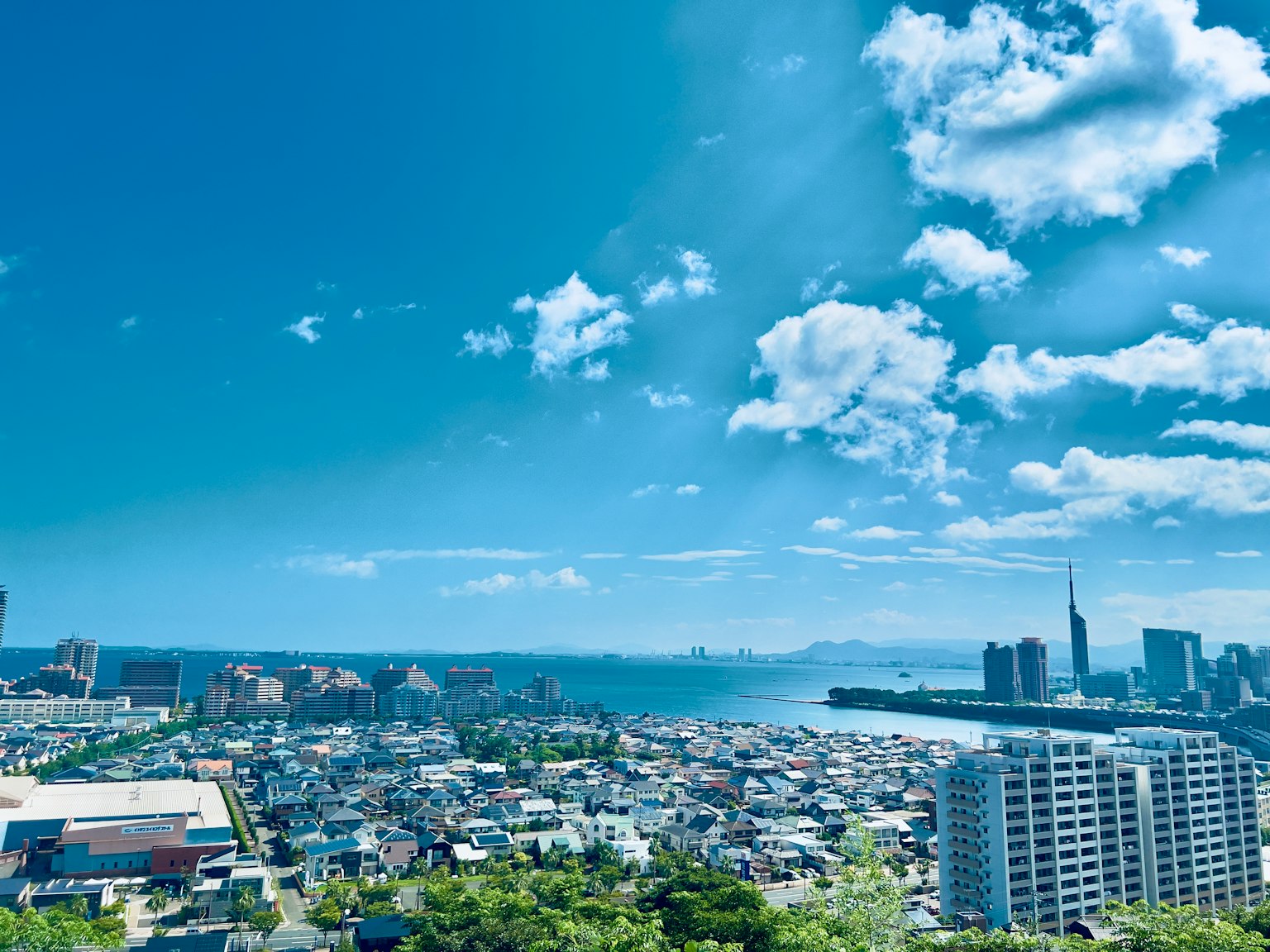 ทิวทัศน์แบบพาโนรามาของเมืองใต้ท้องฟ้าสีฟ้าพร้อมเมฆมีทะเลและตึกระฟ้า