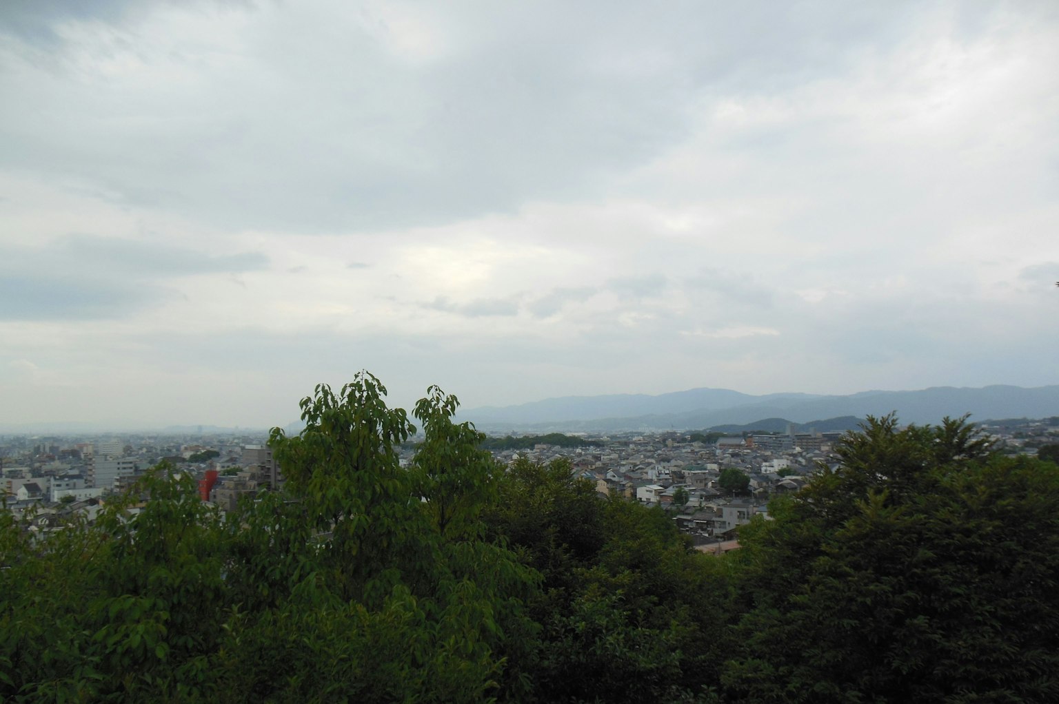 Panorama della città sotto un cielo nuvoloso con alberi verdi e montagne lontane