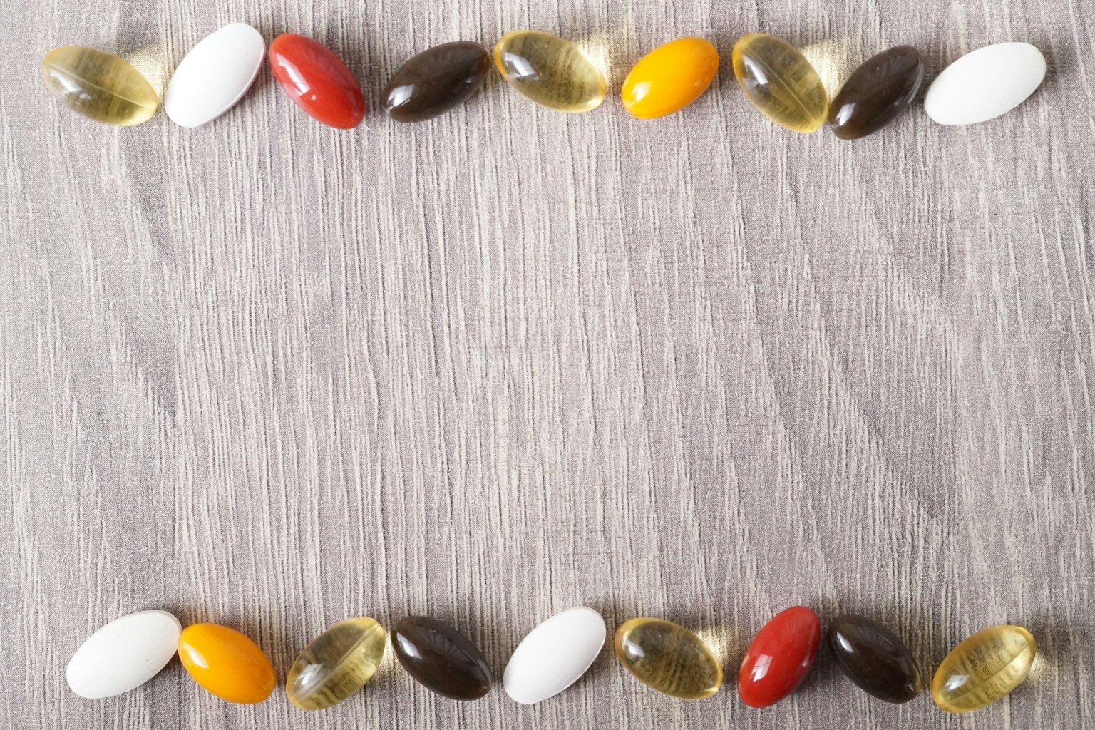Capsule di integratori di diversi colori disposte su uno sfondo di legno