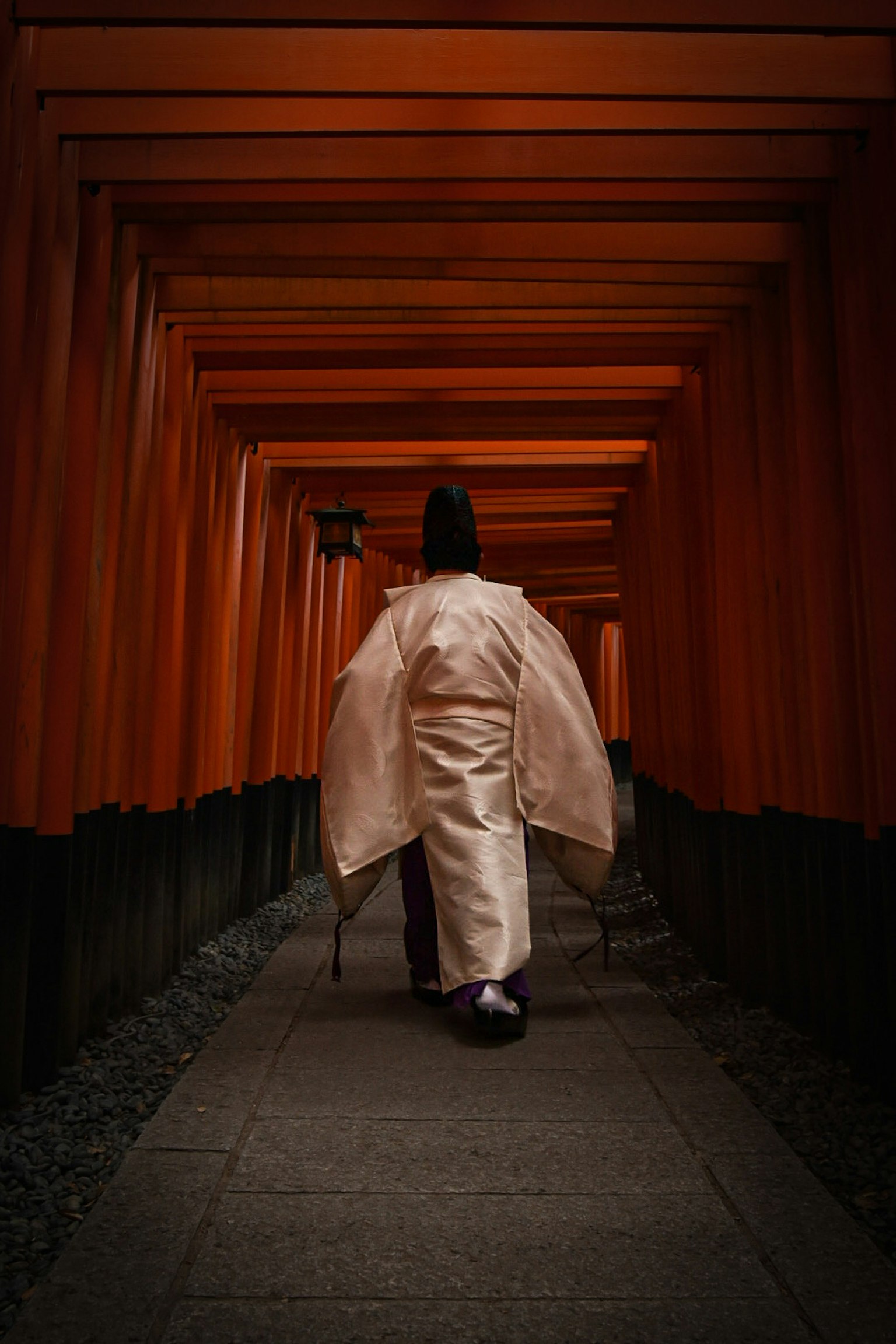 Person in white kimono walking through orange torii gate tunnel