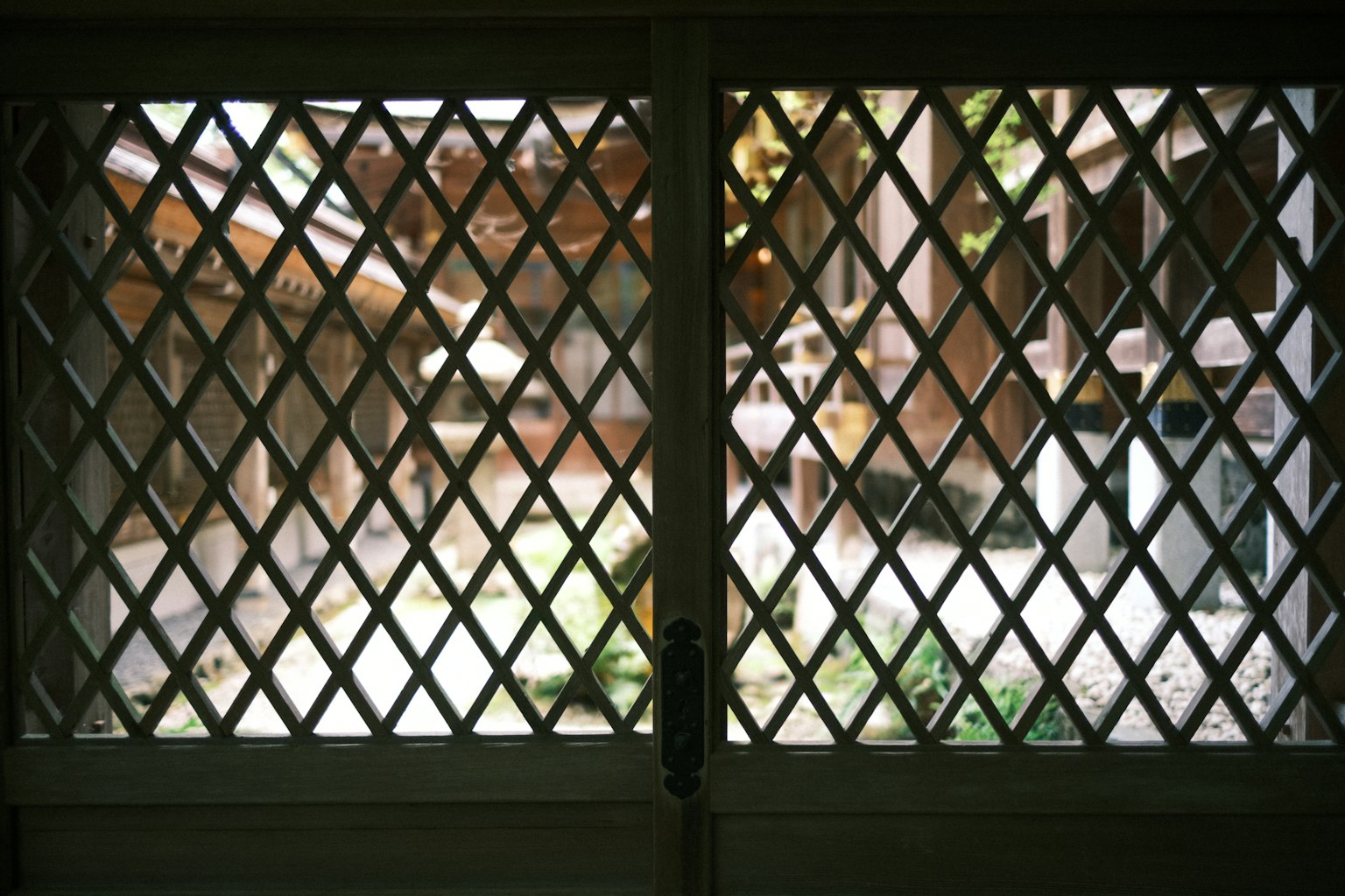 Blick auf einen Innenhof mit Pflanzen durch ein rautenförmiges Fenster