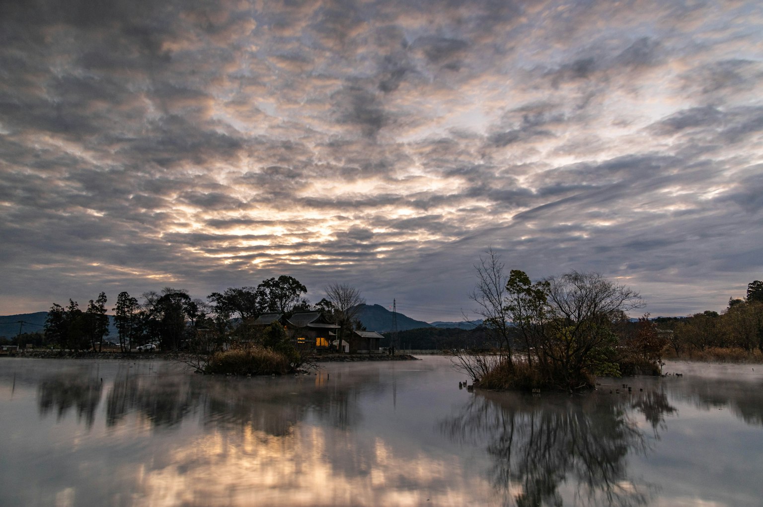 Ruhige Seenlandschaft mit Bergen, die im bewölkten Himmel reflektiert werden
