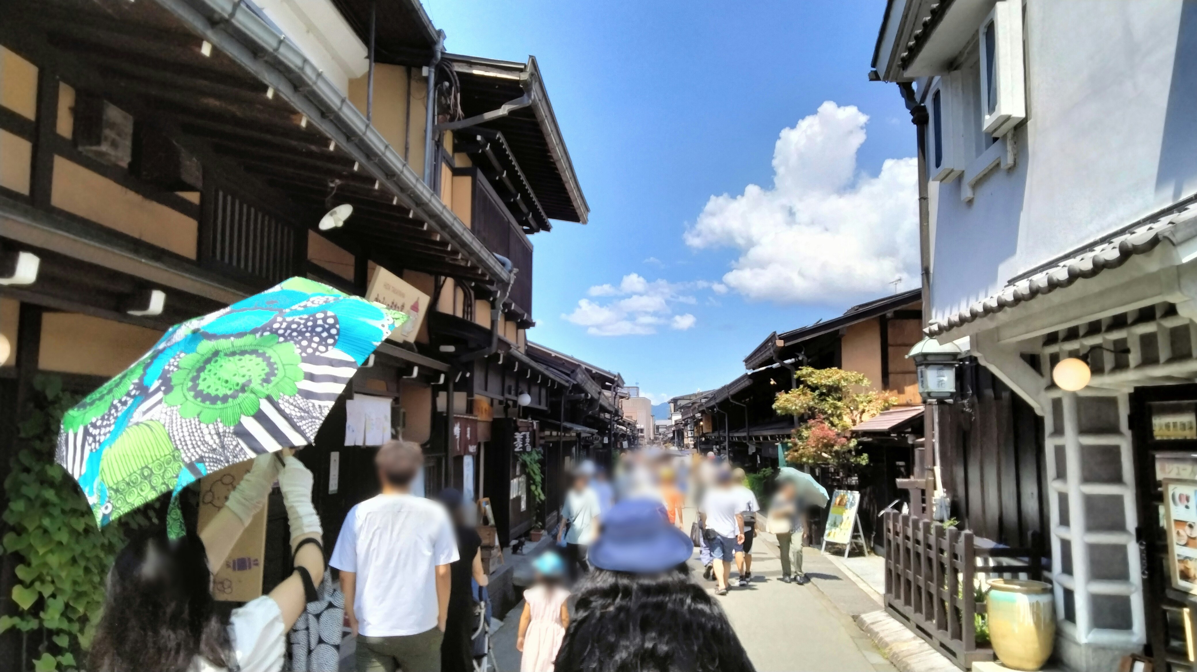 路地に並ぶ軒先と人々、日傘のある商店街の通り