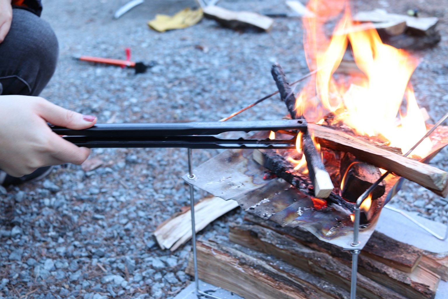 Mano ajustando el fuego con pinzas en un entorno de fogata