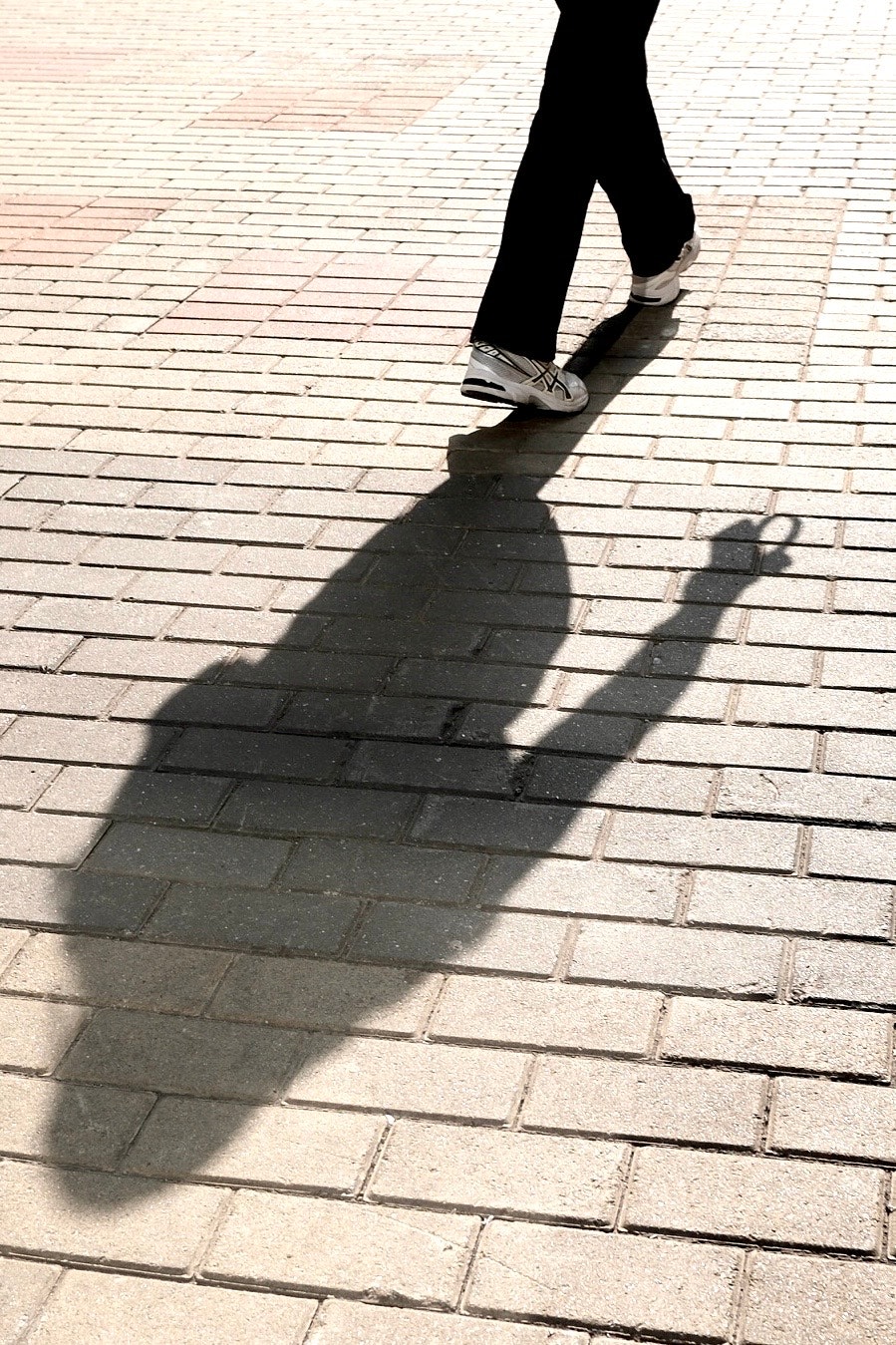 レンガ敷きの歩道を歩く人の影