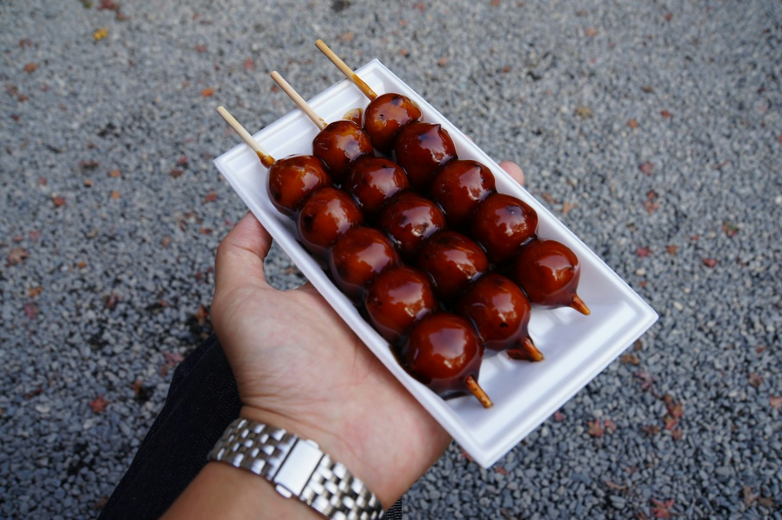 A hand holding a plate of skewered sweet dango balls